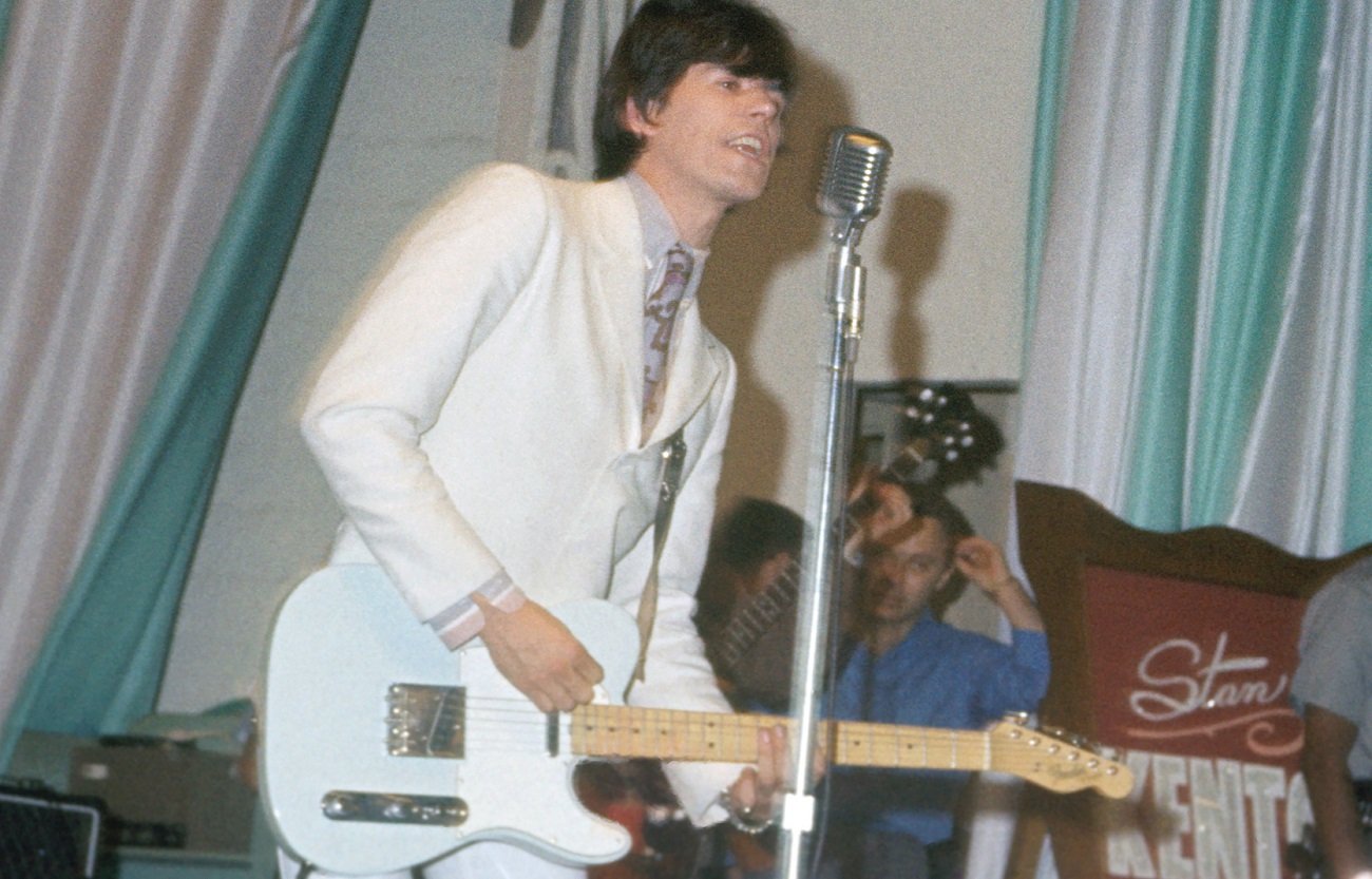 Keith Richards sings into a microphone and plays a Fender guitar on stage in 1966.