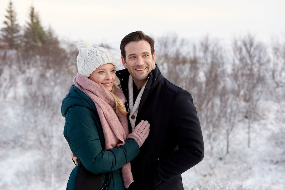 Woman in white hat and green coat with her arms around man in black coat in Hallmark Channel movie Love on Icelance