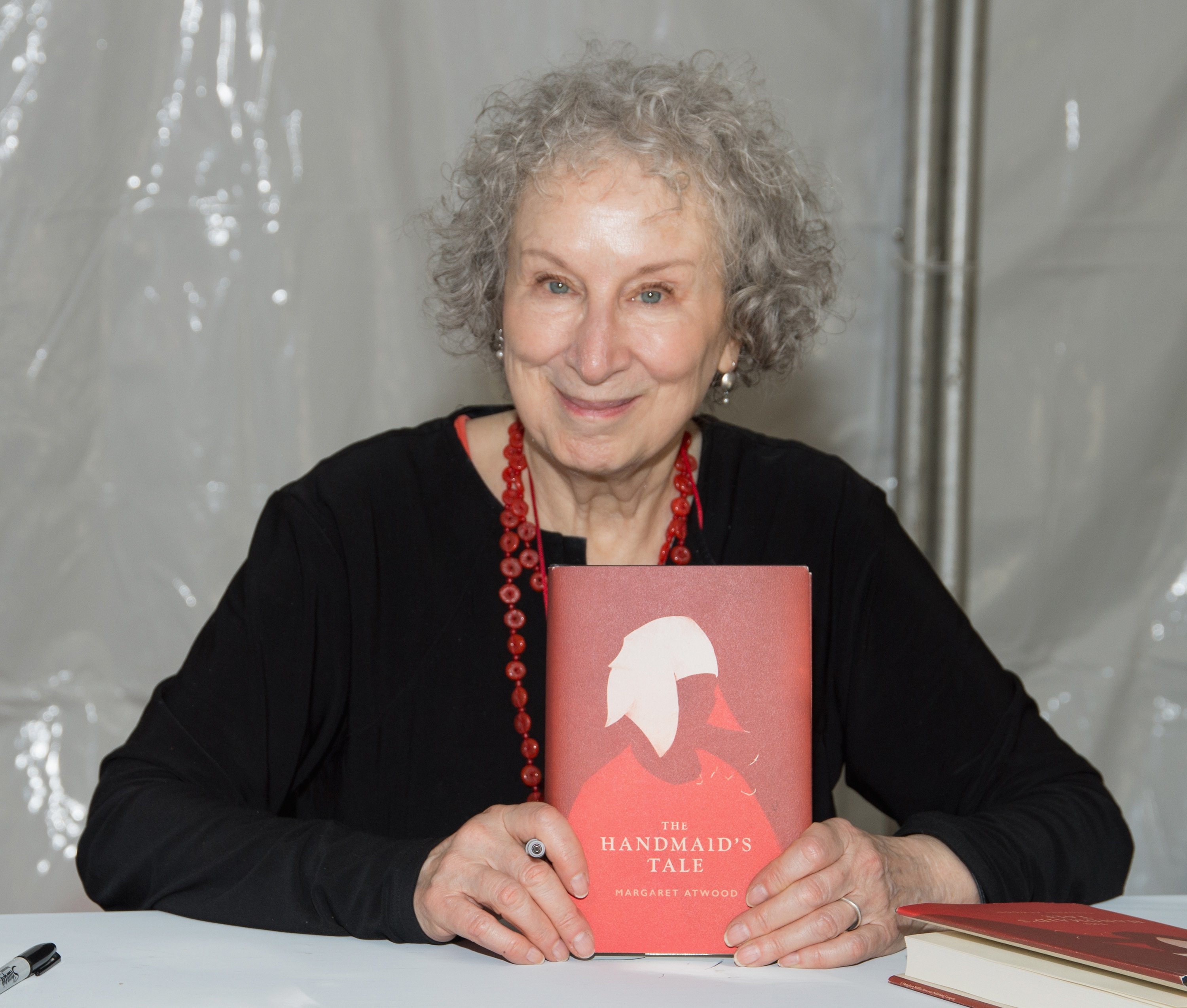 Margaret Atwood sitting and holding a copy of The Handmaids Tale