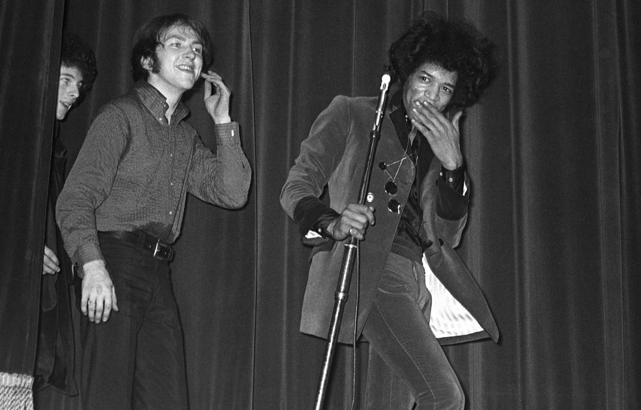 Jimi Hendrix smiles and covers his mouth as he walks on stage with Mitch Mitchell