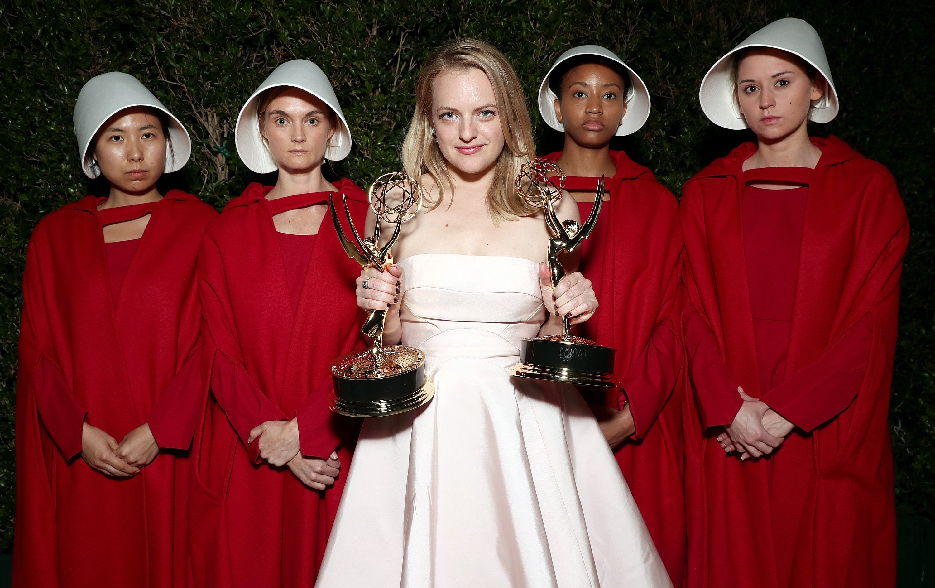 Elisabeth Moss with awards surrounded by women dressed in Handmaid's Tale outfits