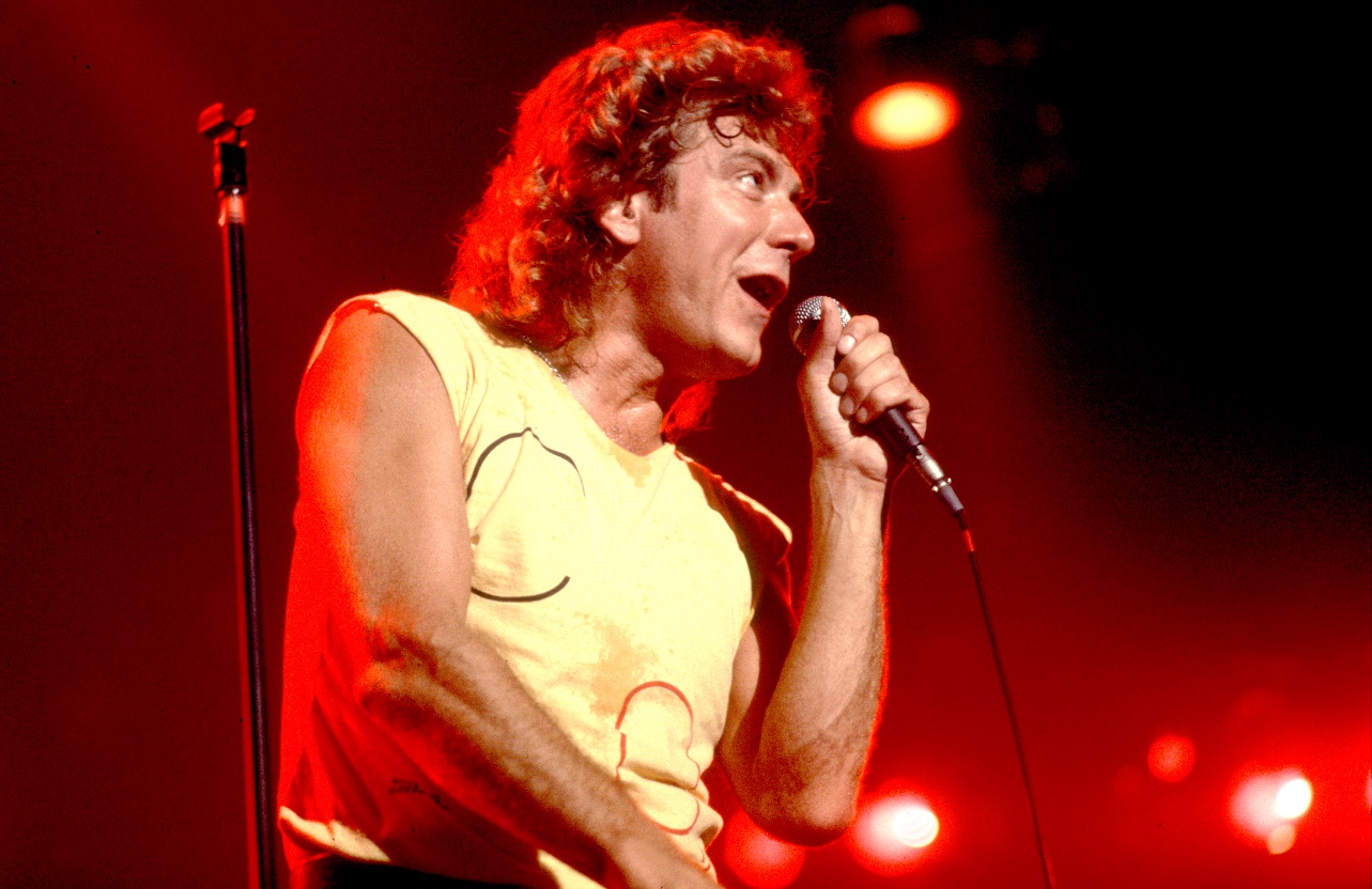 Robert Plant smiles and sings into a microphone on stage in 1985.