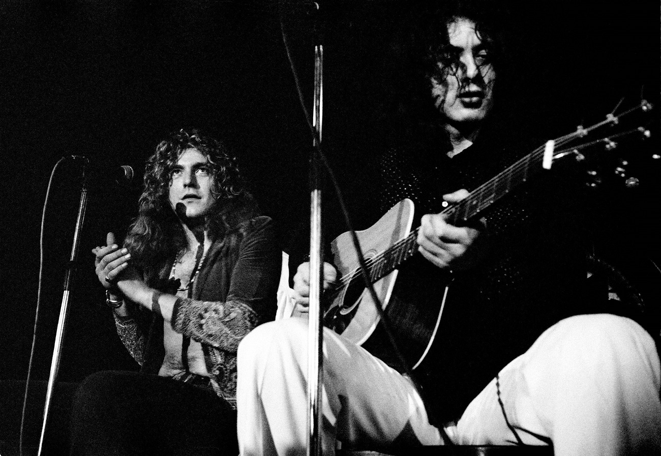Robert Plant claps his hands as Jimmy Page, seated next to him, plays guitar.