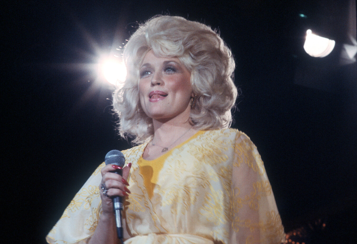 Dolly Parton performs onstage wearing a yellow dress in 1975 in Los Angeles, California.