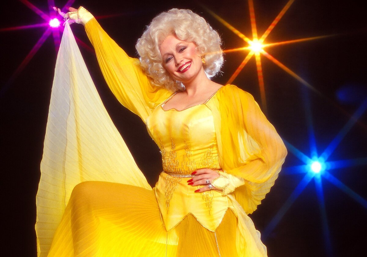 Dolly Parton poses for a portrait in a bright yellow dress with her signature big blonde hair.
