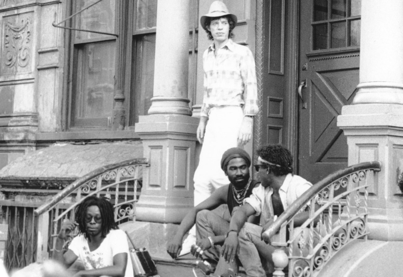 Mick Jagger stands on the stoop of a New York building while shooting a music video