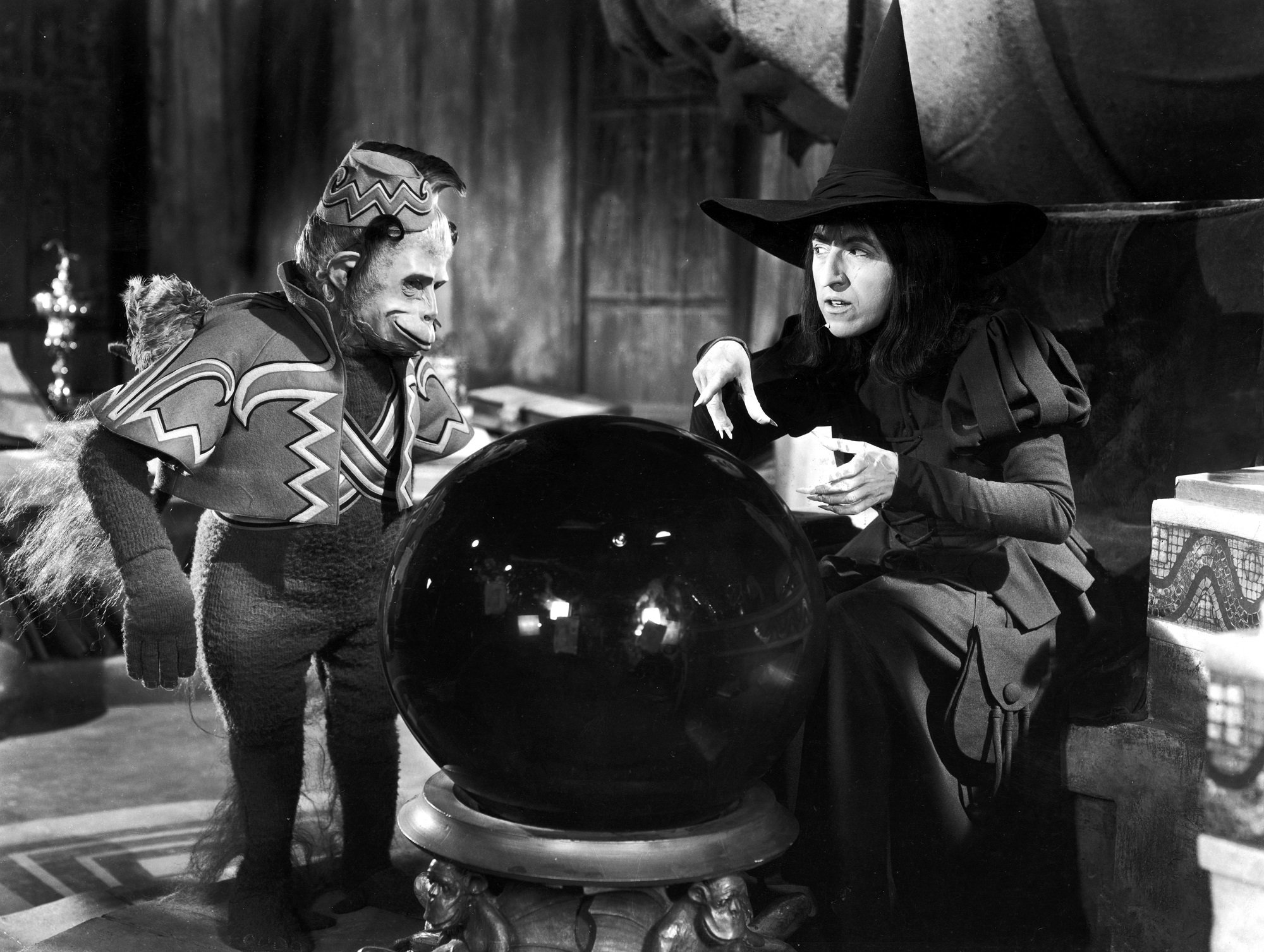 American actor Margaret Hamilton (1902 - 1985) and a winged monkey look into a crystal ball in a still from the film, The Wizard of Oz, directed by Victor Fleming, 1939