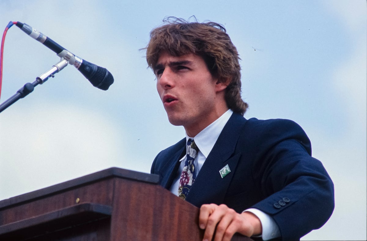Tom Cruise wears a suit and speaks at a podium at the United States Capitol in 1990