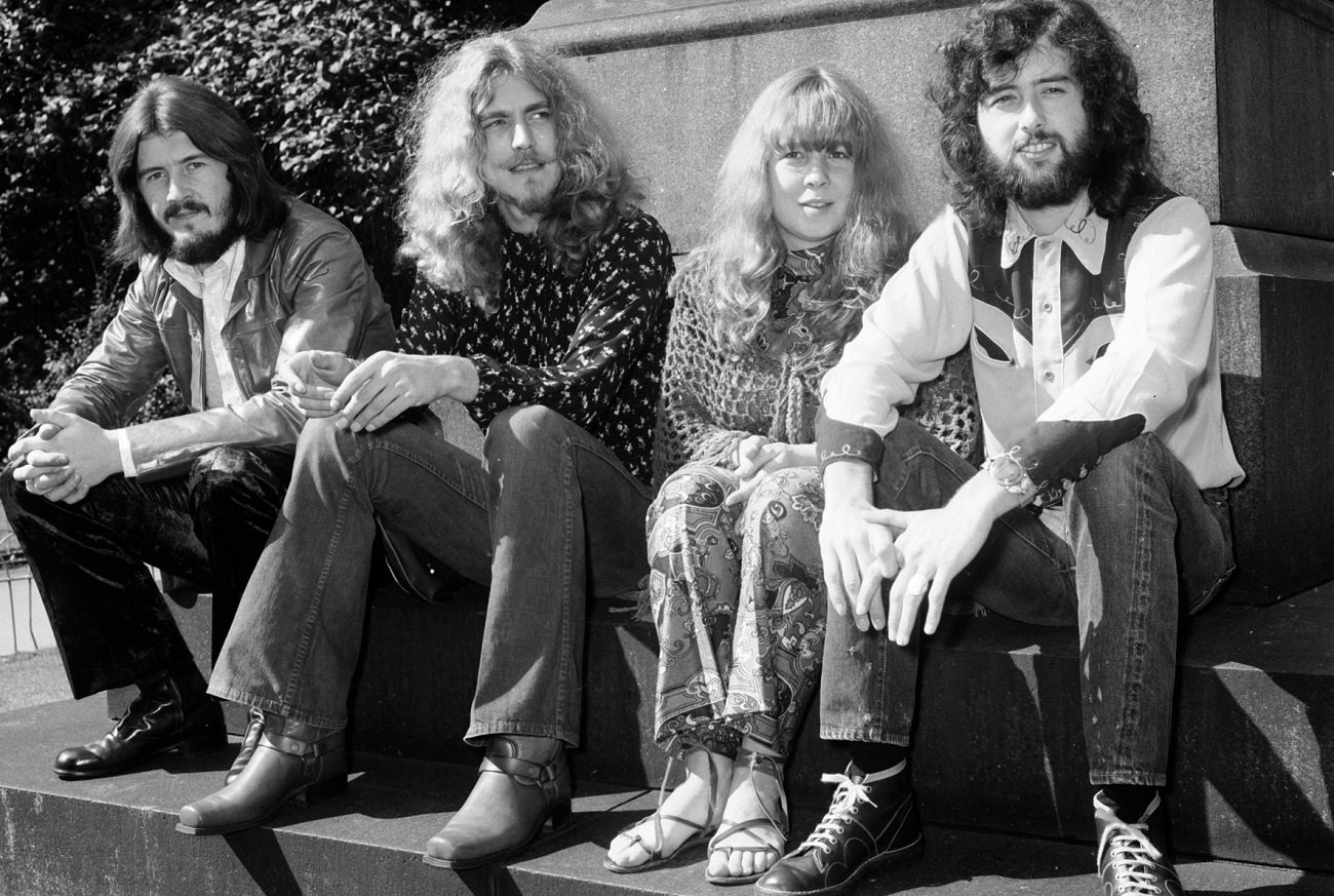 John Bonham, Robert Plant, Sandy Denny, and Jimmy Page posing together, seated, at the base of a statue