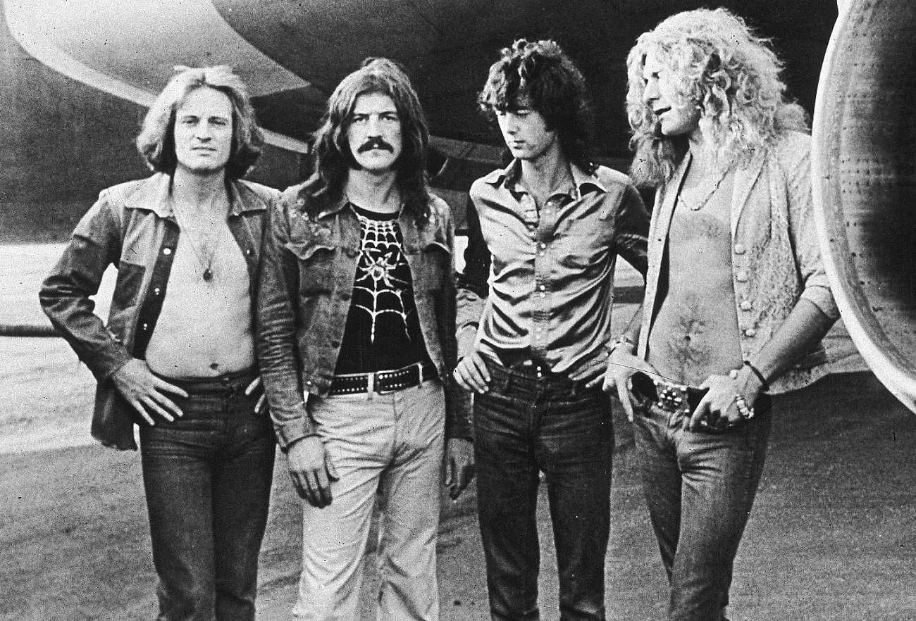 Members of Led Zeppelin posing in front of the jet engine of their private plane