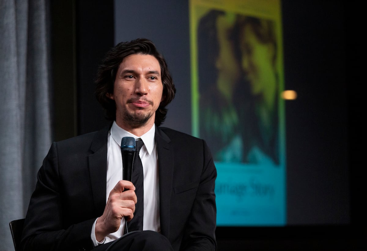 Adam Driver wears a suit, holds a microphone, and smiles at a 'Marriage Story' screening