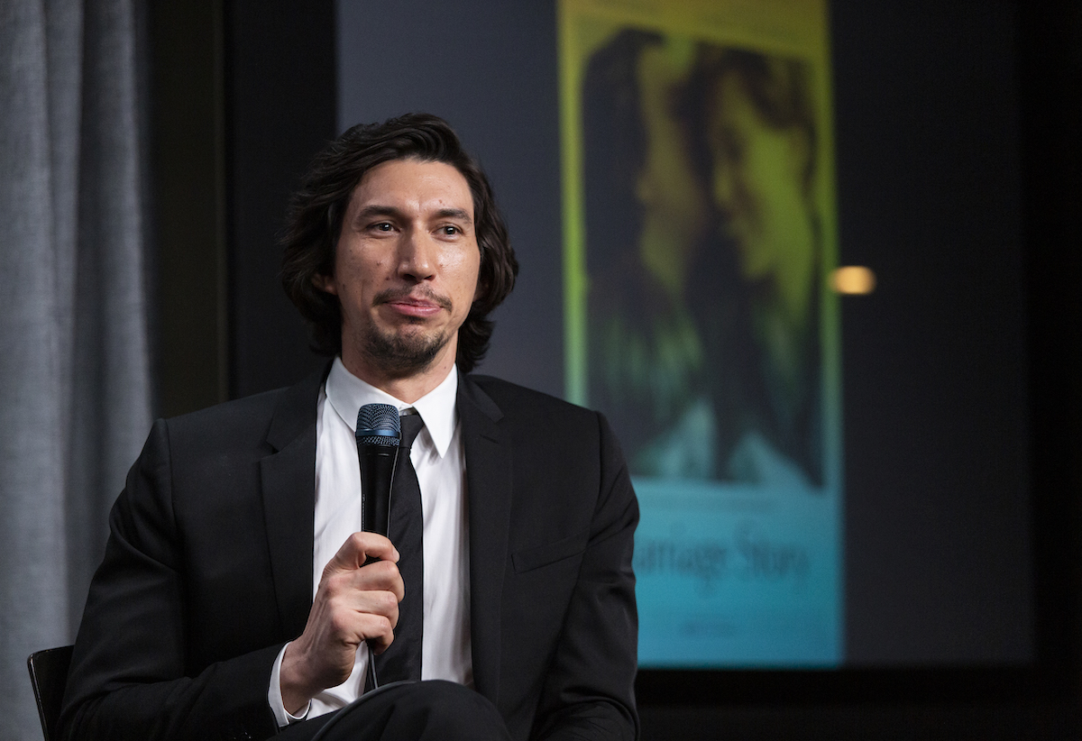 Adam Driver wears a suit, holds a microphone, and smiles at a 'Marriage Story' screening