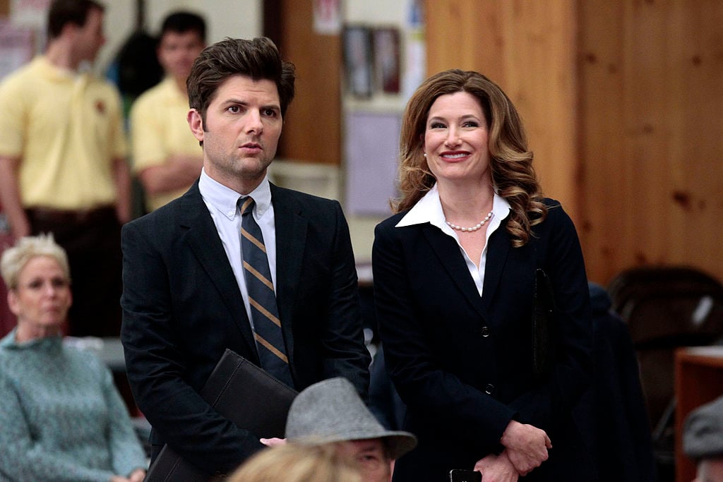 Adam Scott as Ben Wyatt, Kathryn Hahn as Jennifer Barkley watch on as they sit next to each other.