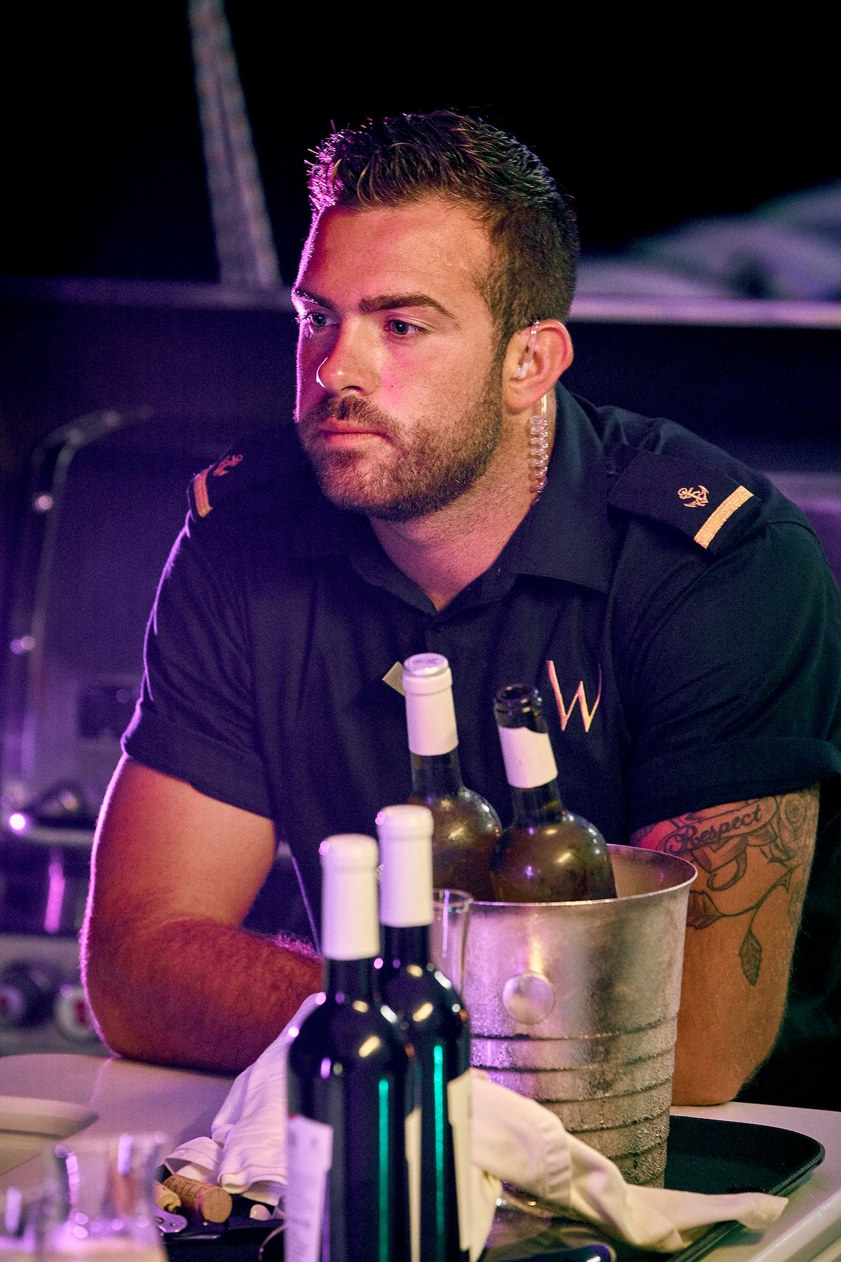 Alex Radcliffe sits at a dinner table in his Below Deck Mediterranean Season 5 uniform