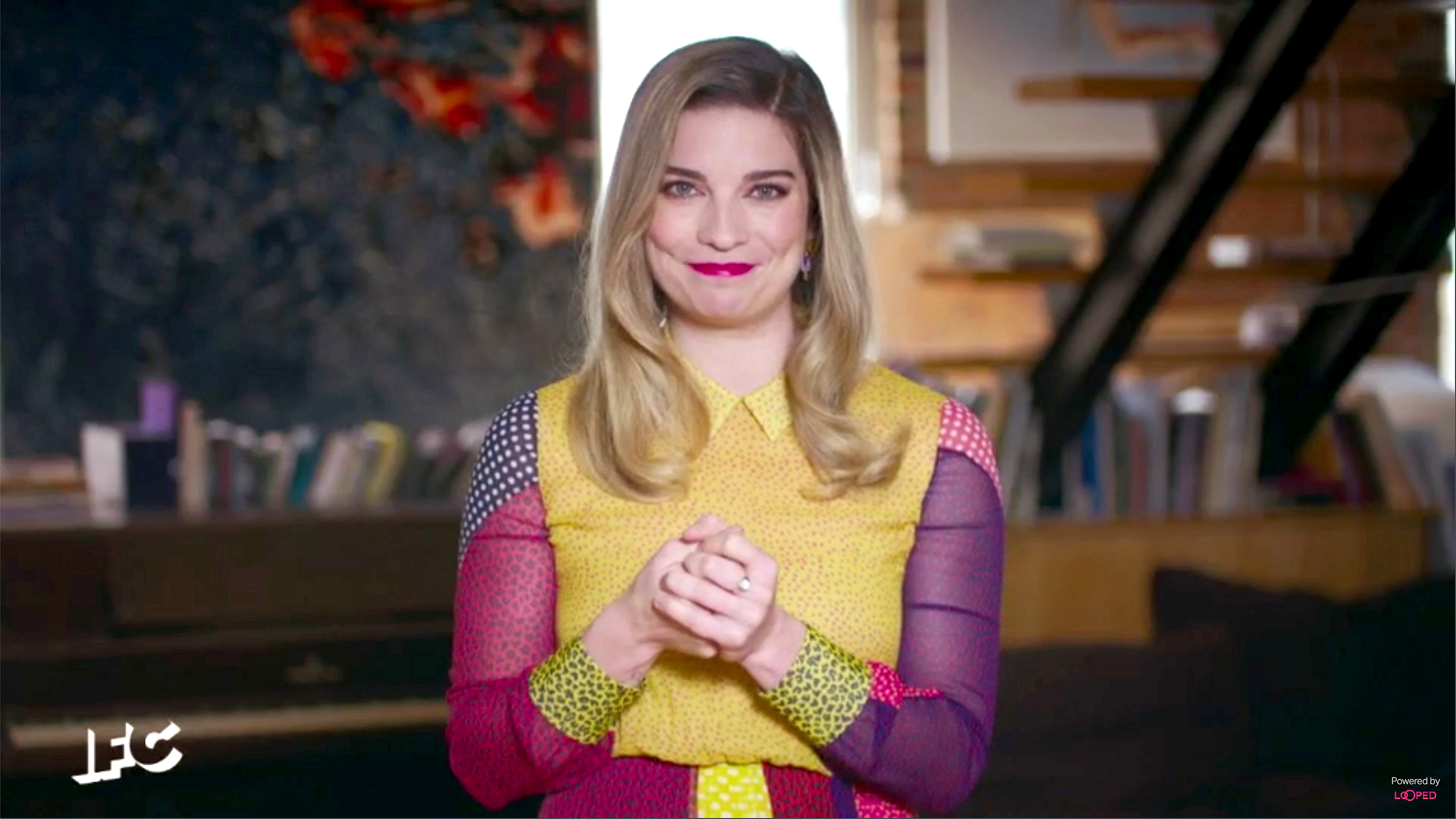 Annie Murphy smiles and claps her hands in a colorful dress and red lipstick