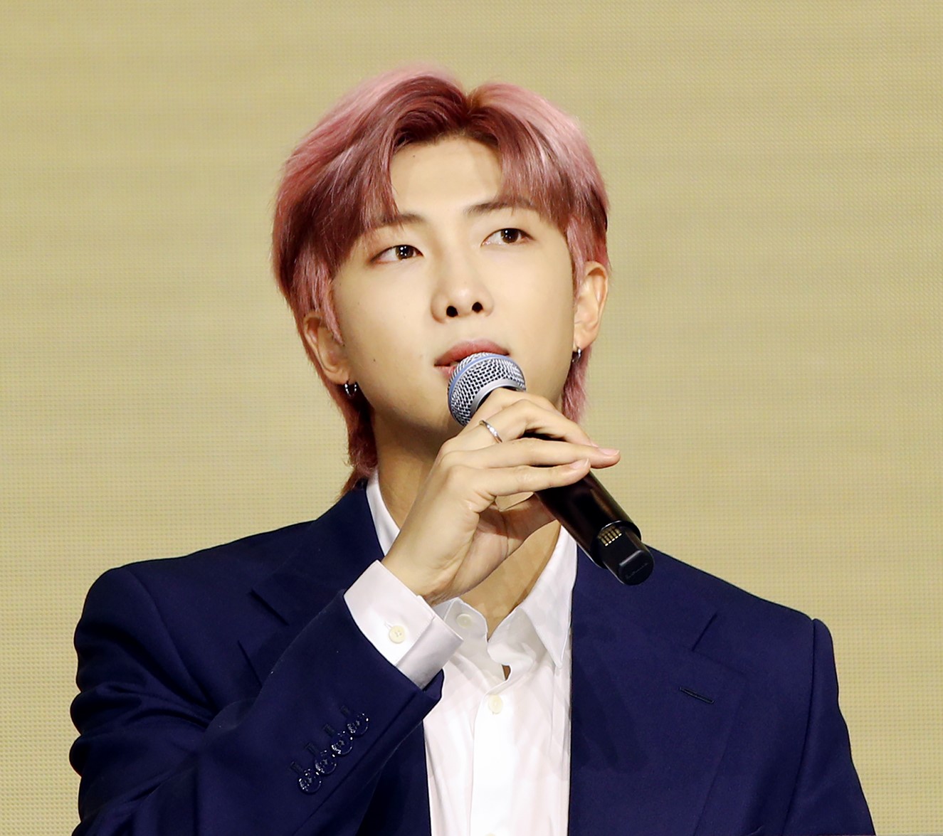 RM of BTS in a blue suit jacket and white shirt holding a microphone