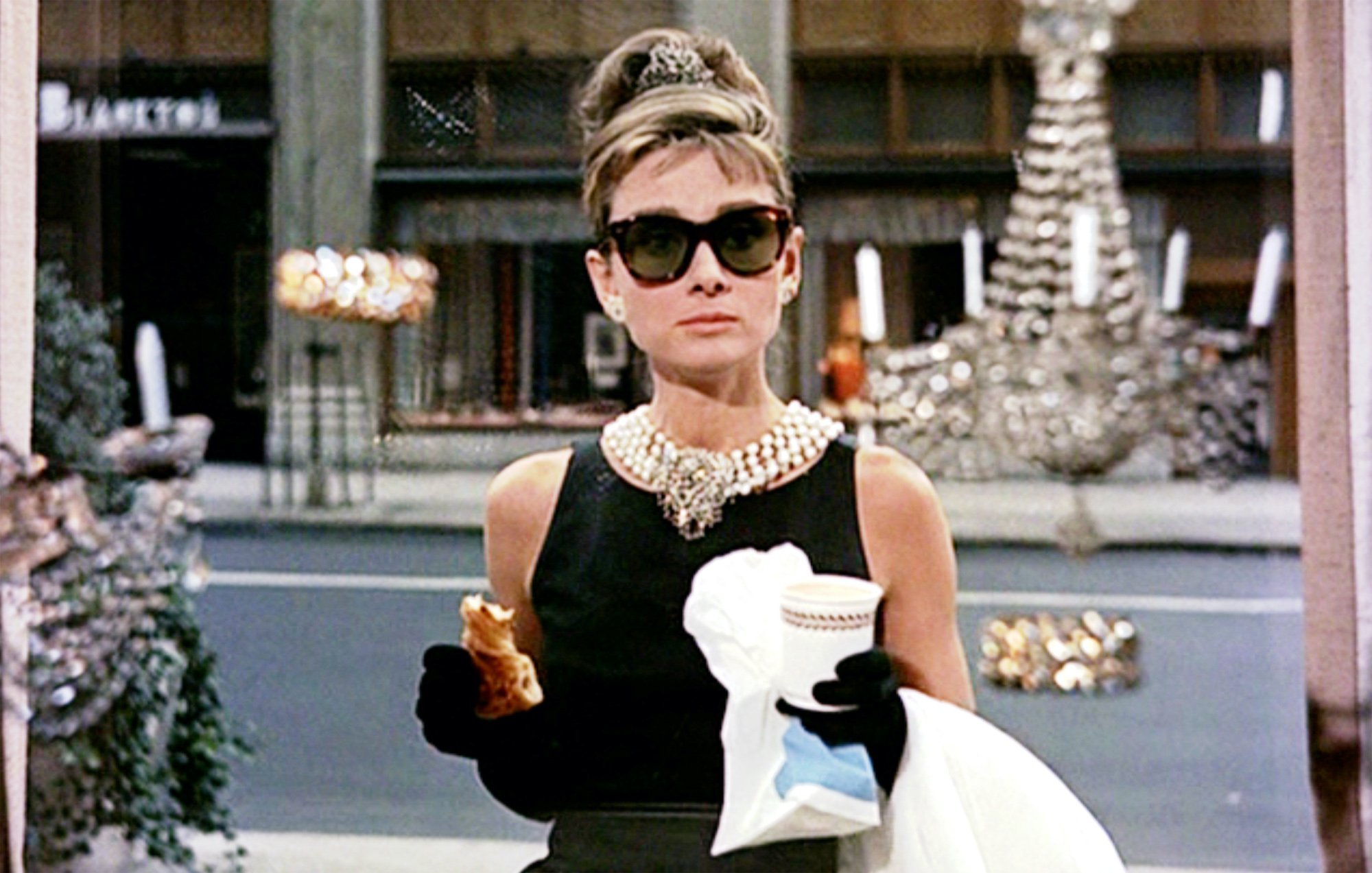 Audrey Hepburn in 'Breakfast at Tiffany's' standing in front of a window holding coffee