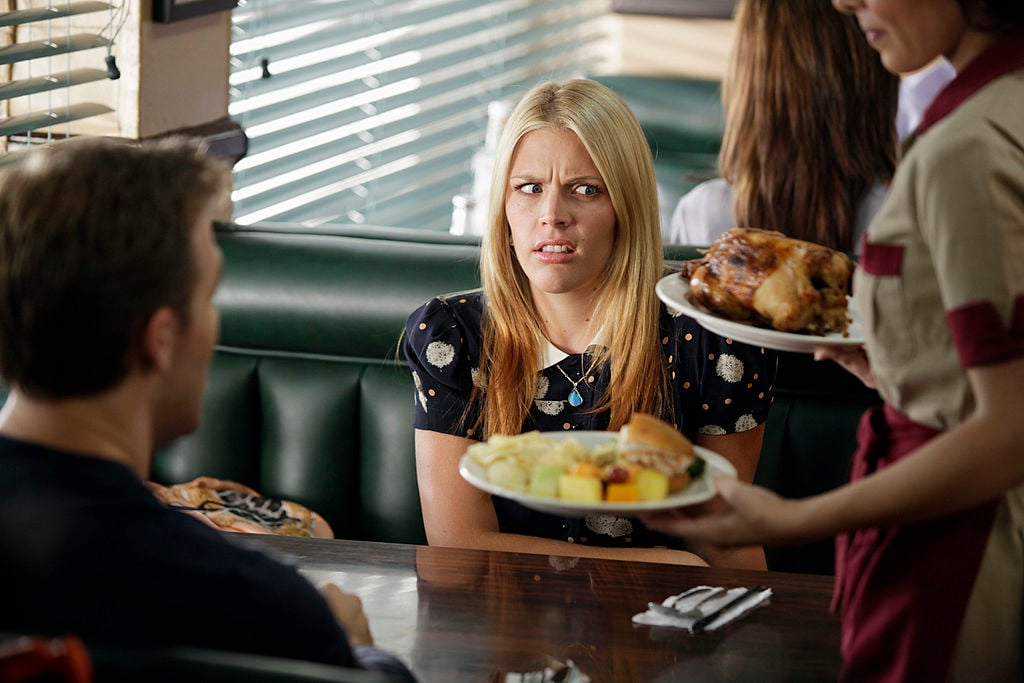 Busy Philipps and James Van der Beek sit in a cafe. Busy has a disgusted look on her face.