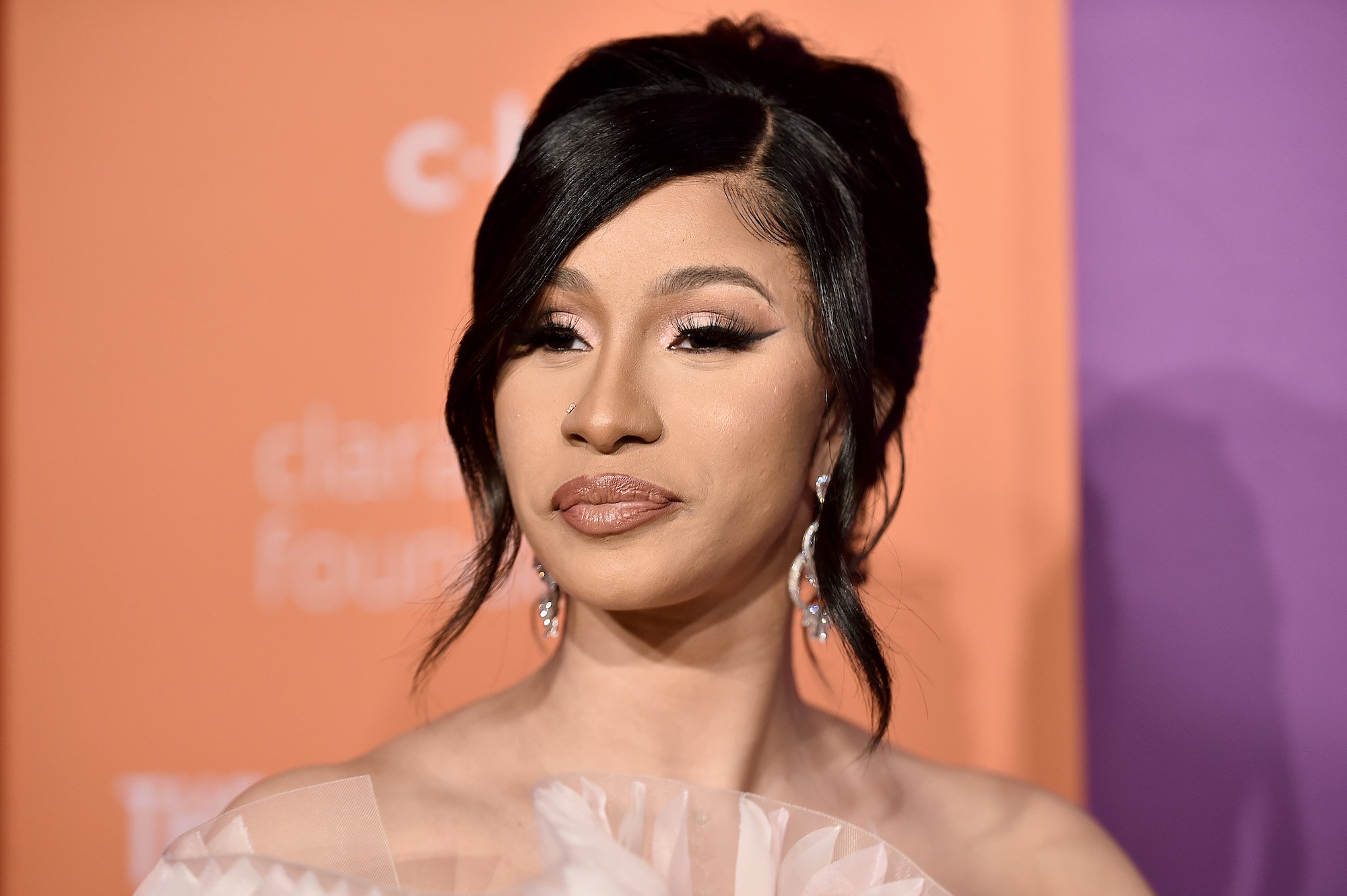 Cardi B smiling in front of an orange and purple background