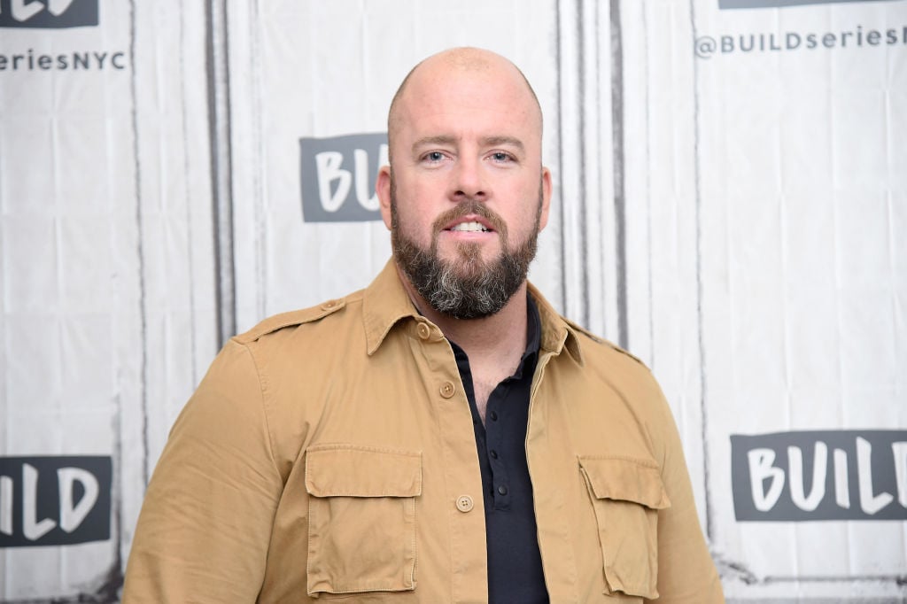 Chris Sullivan walks the red carpet in a black shirt and tan jacket.