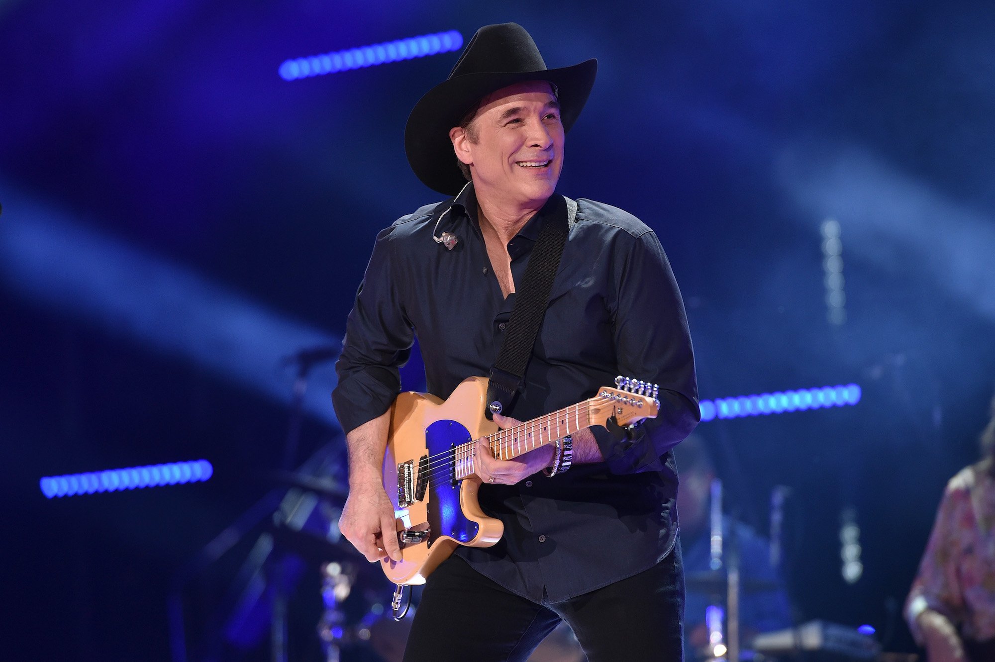 Clint Black smiling, holding a guitar on stage