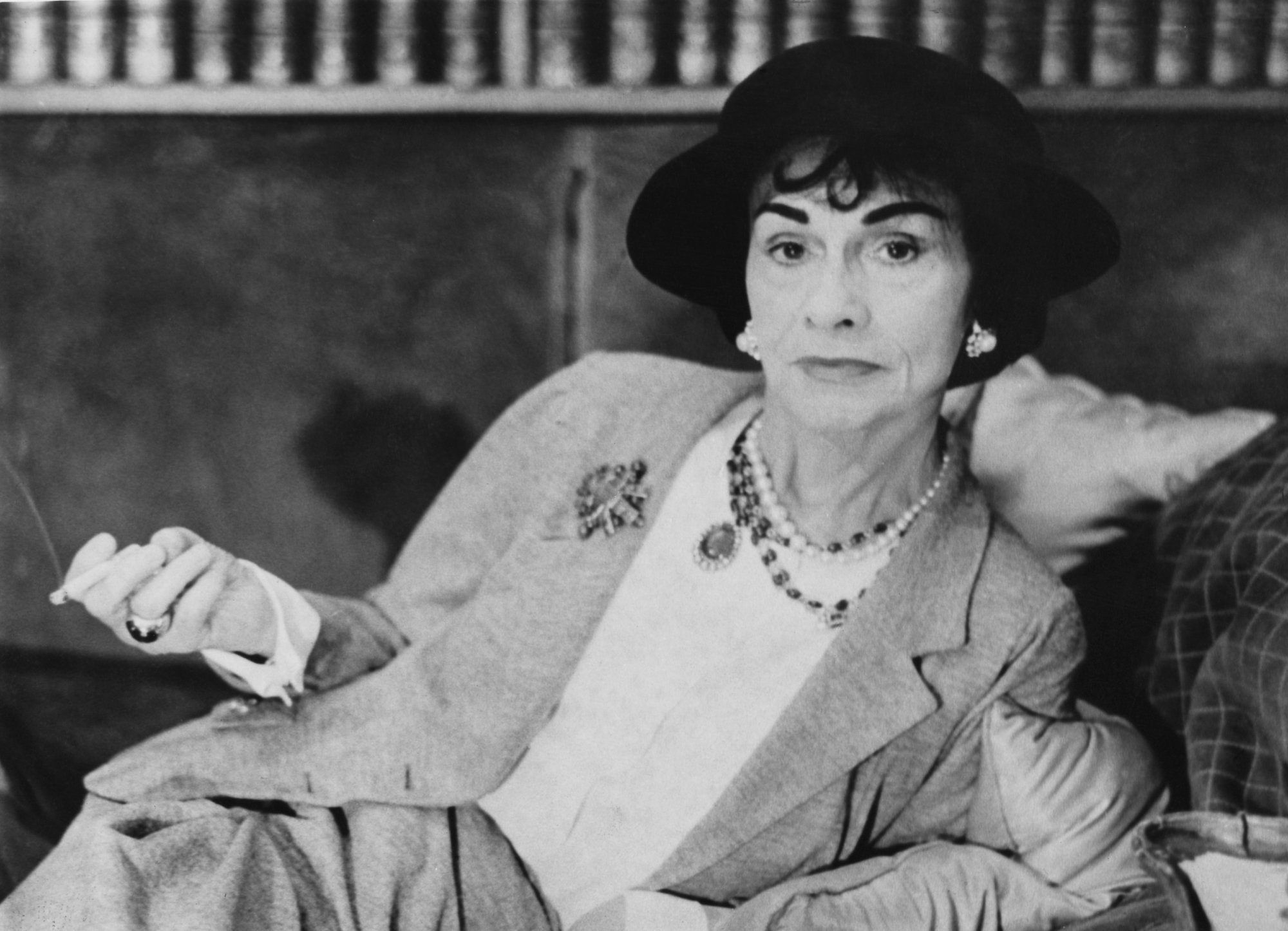Coco Chanel sitting on a couch, in black and white