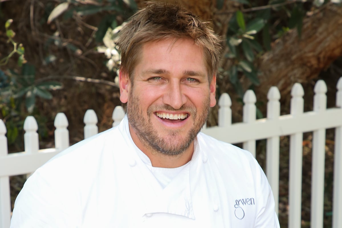 Curtis Stone wears a chef's coat and smiles at the camera.