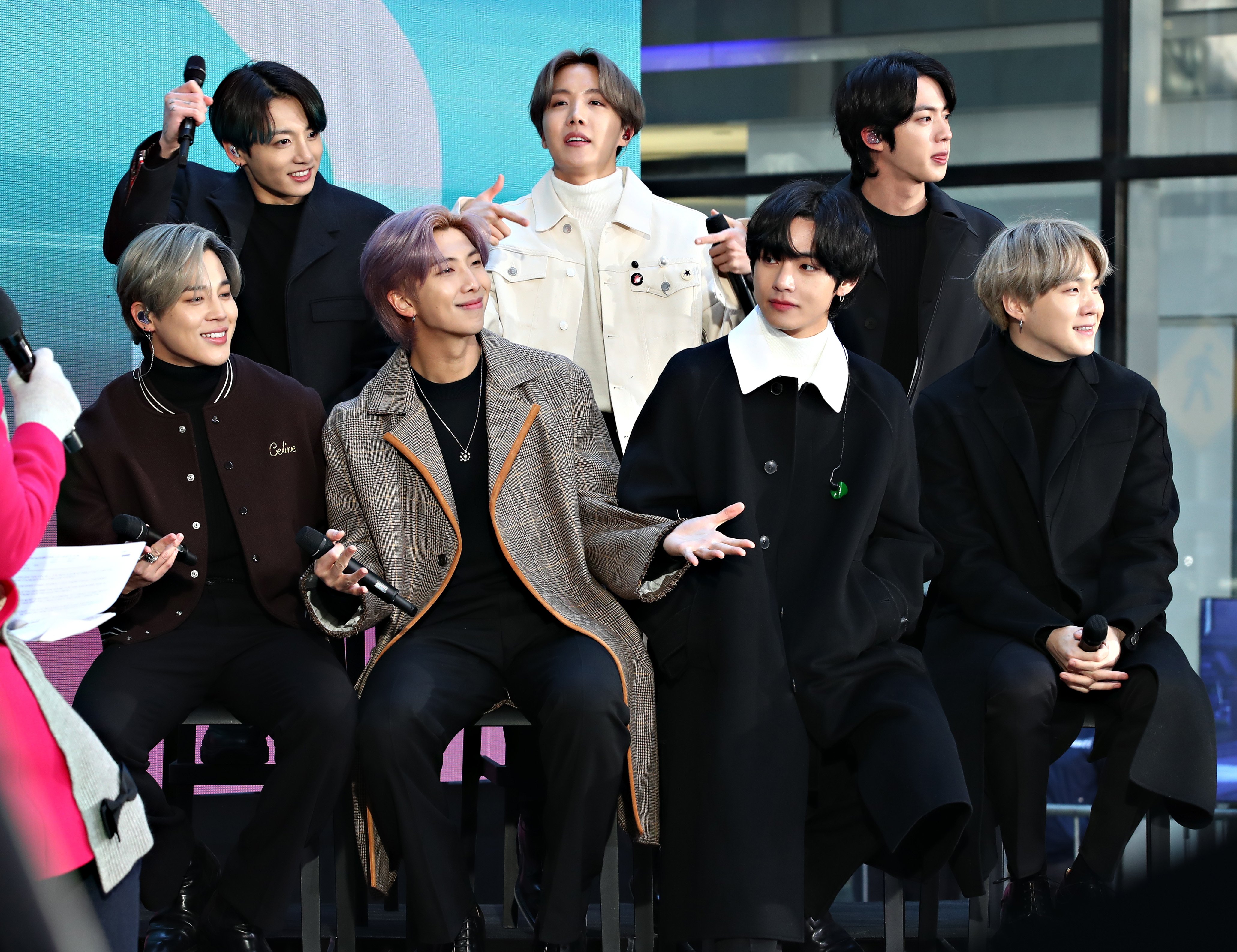 Jimin, Jungkook, RM, J-Hope, V, Jin, and Suga of the K-pop boy band BTS sitting together on stage in winter coats