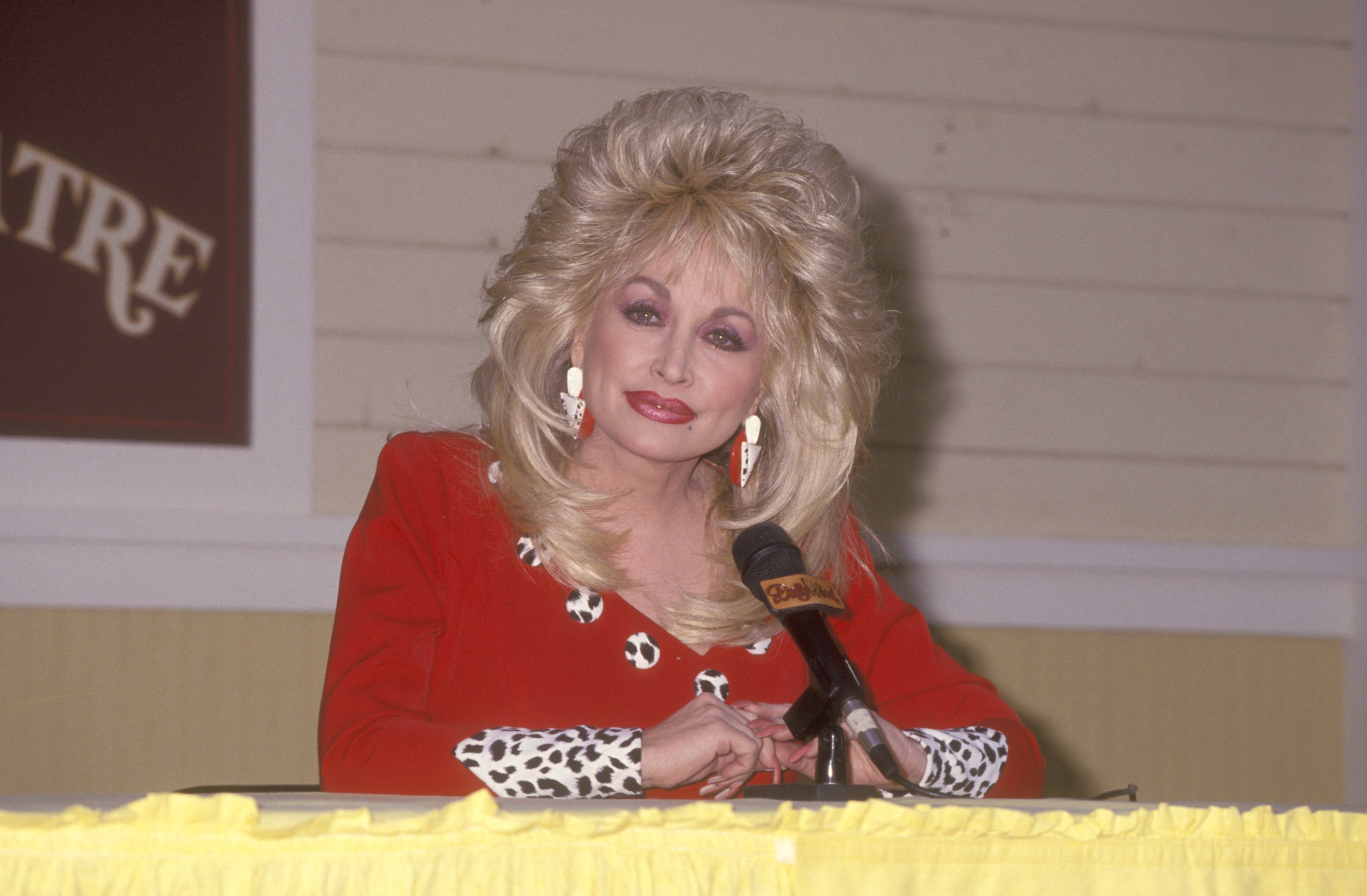 Dolly Parton sits in front of a microphone in a red dress at the Opening Weekend Celebration of Dollywood on April 24, 1993 at Dollywood in Pigeon Forge, Tennessee.