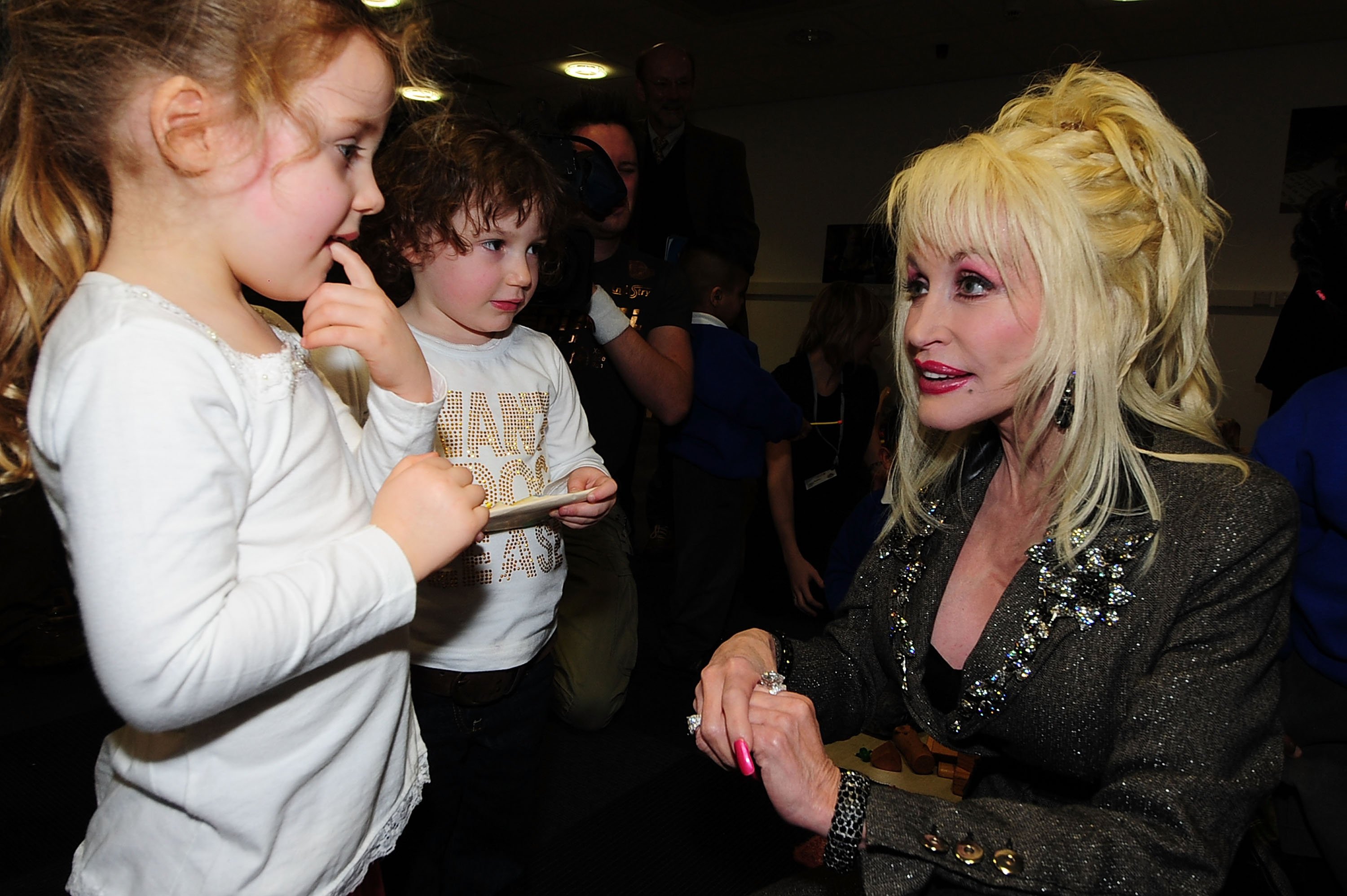 Dolly Parton kneels down to talk to two children at an Imagination Library event.