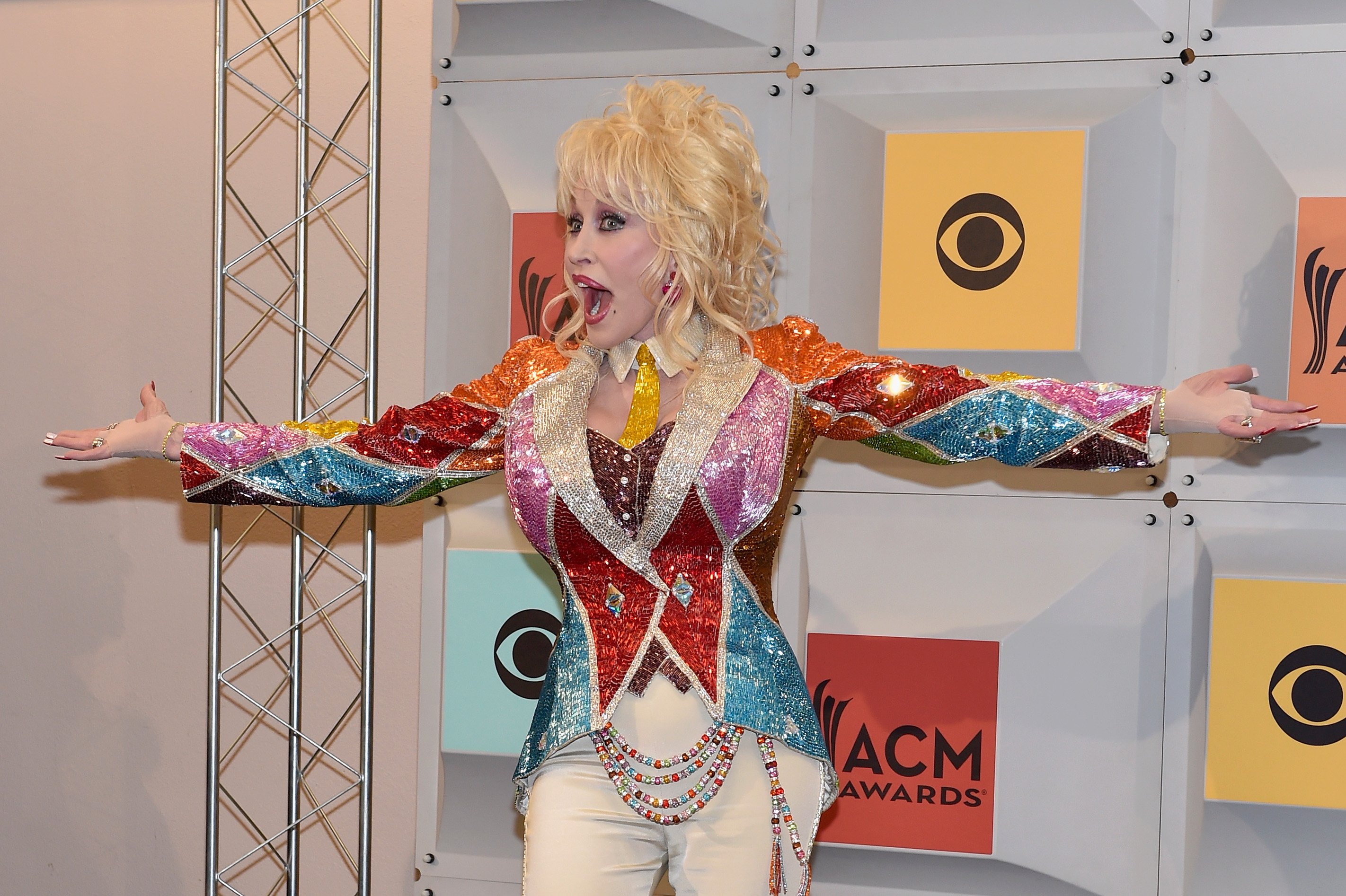 Dolly Parton excitedly poses for photos in a sparkly, multi-colored suit.