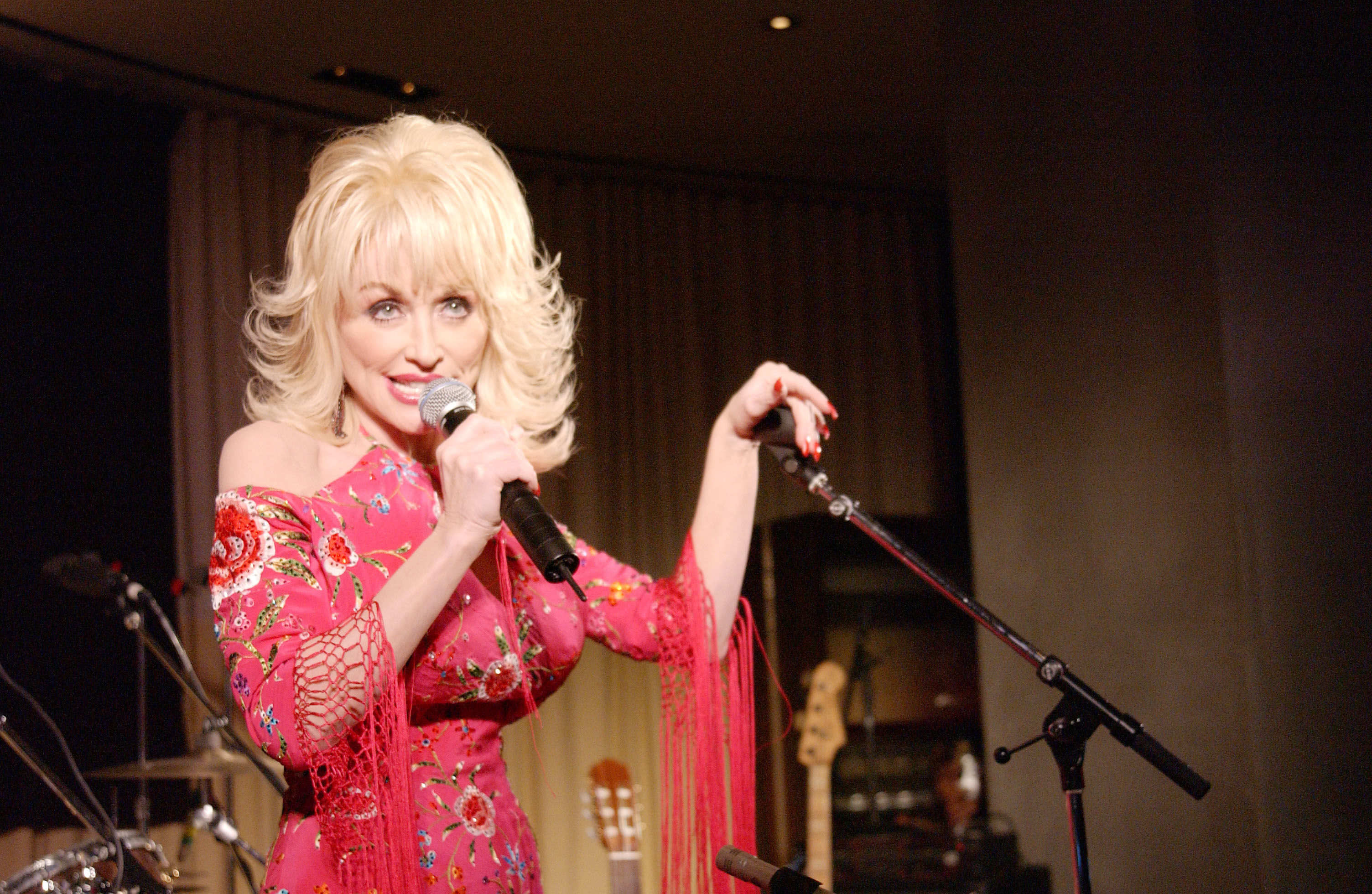 Dolly Parton performing on stage. She's in a red dress and singing into a microphone, smiling.
