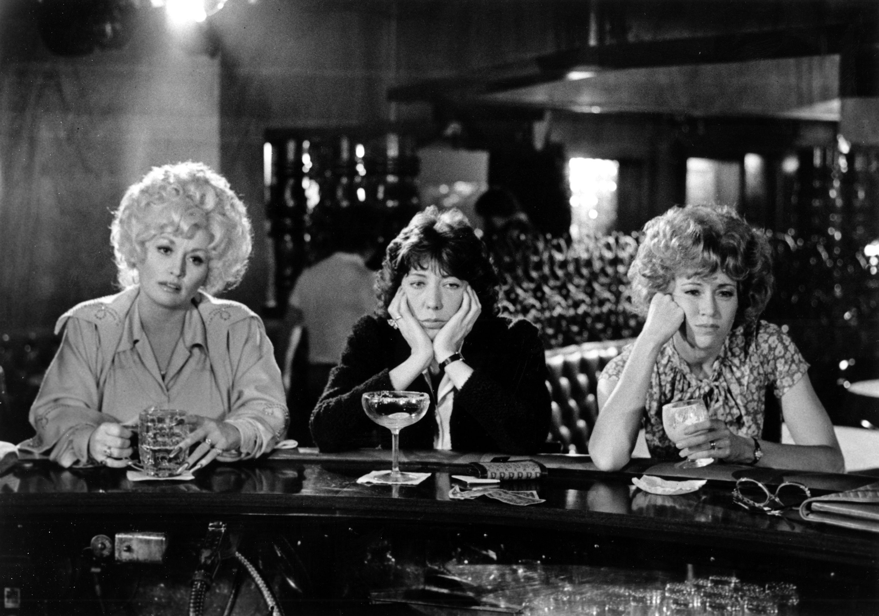 Dolly Parton, Lily Tomlin and Jane Fonda sit at a bar in a film still from '9 to 5.'