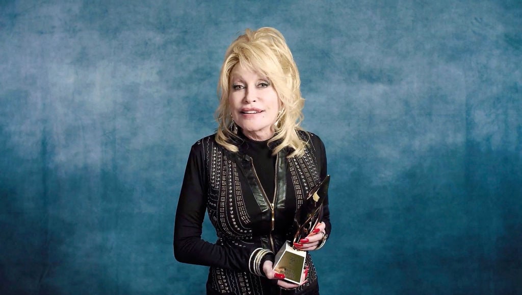 Dolly Parton accepts the Hitmaker Award while wearing a black dress as she holds a trophy