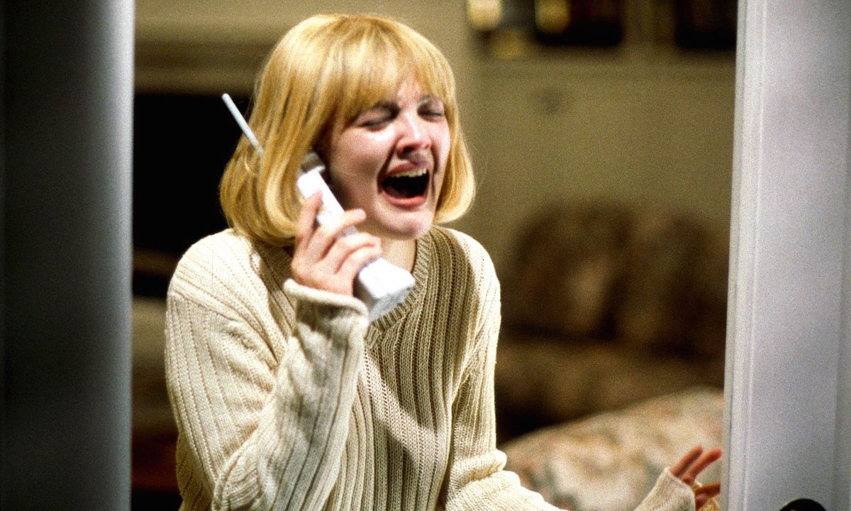 Casey Becker (Drew Barrymore) wears a white sweater and screams while holding a phone in 'Scream'