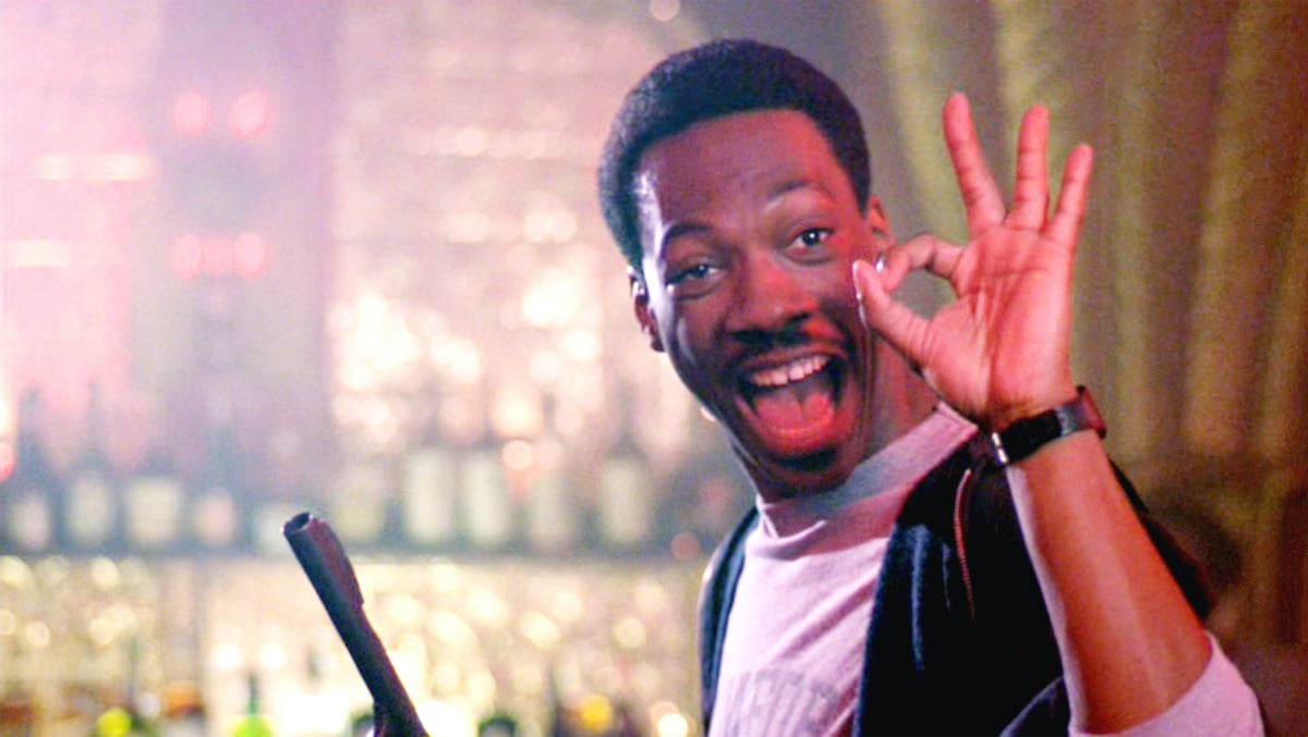 Eddie Murphy as Axel Foley in 'Beverly Hills Cop' makes the okay sign with his hand while holding a gun