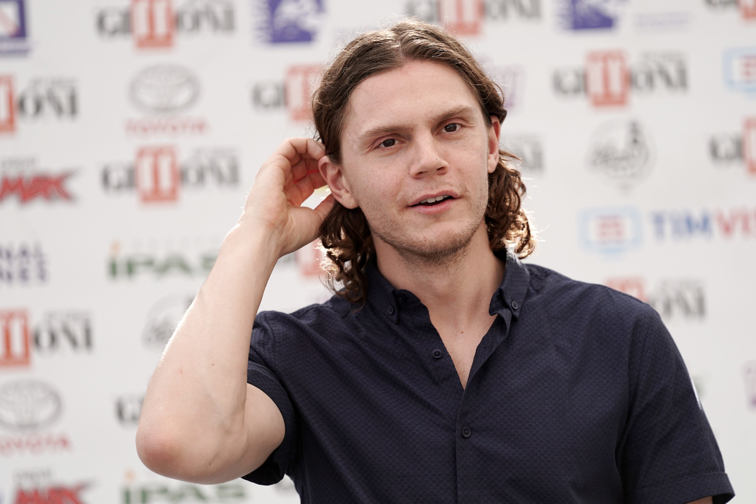 Evan Peters wears a black shirt and pushes his hair behind his ear during the Giffoni Film Festival