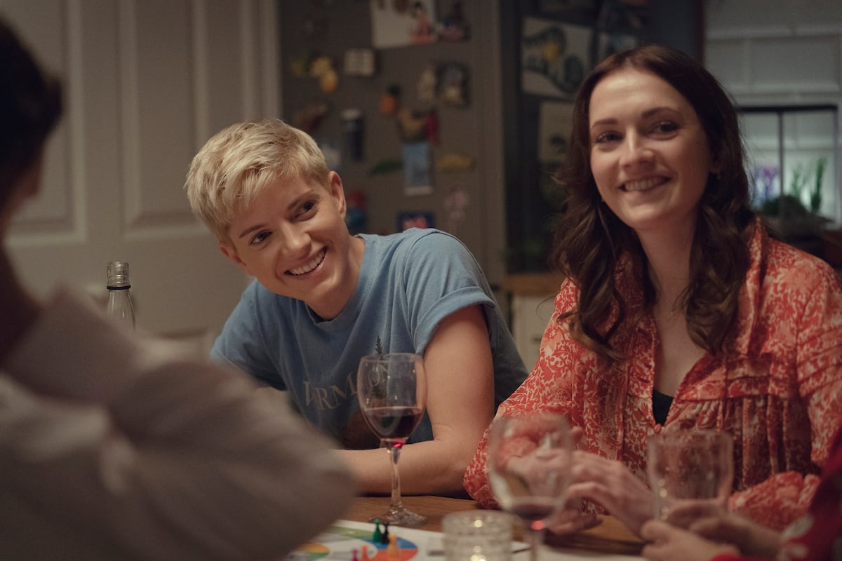 Mae Martin and Charlotte Ritchie sit at a dinner table smiling on 'Feel Good'