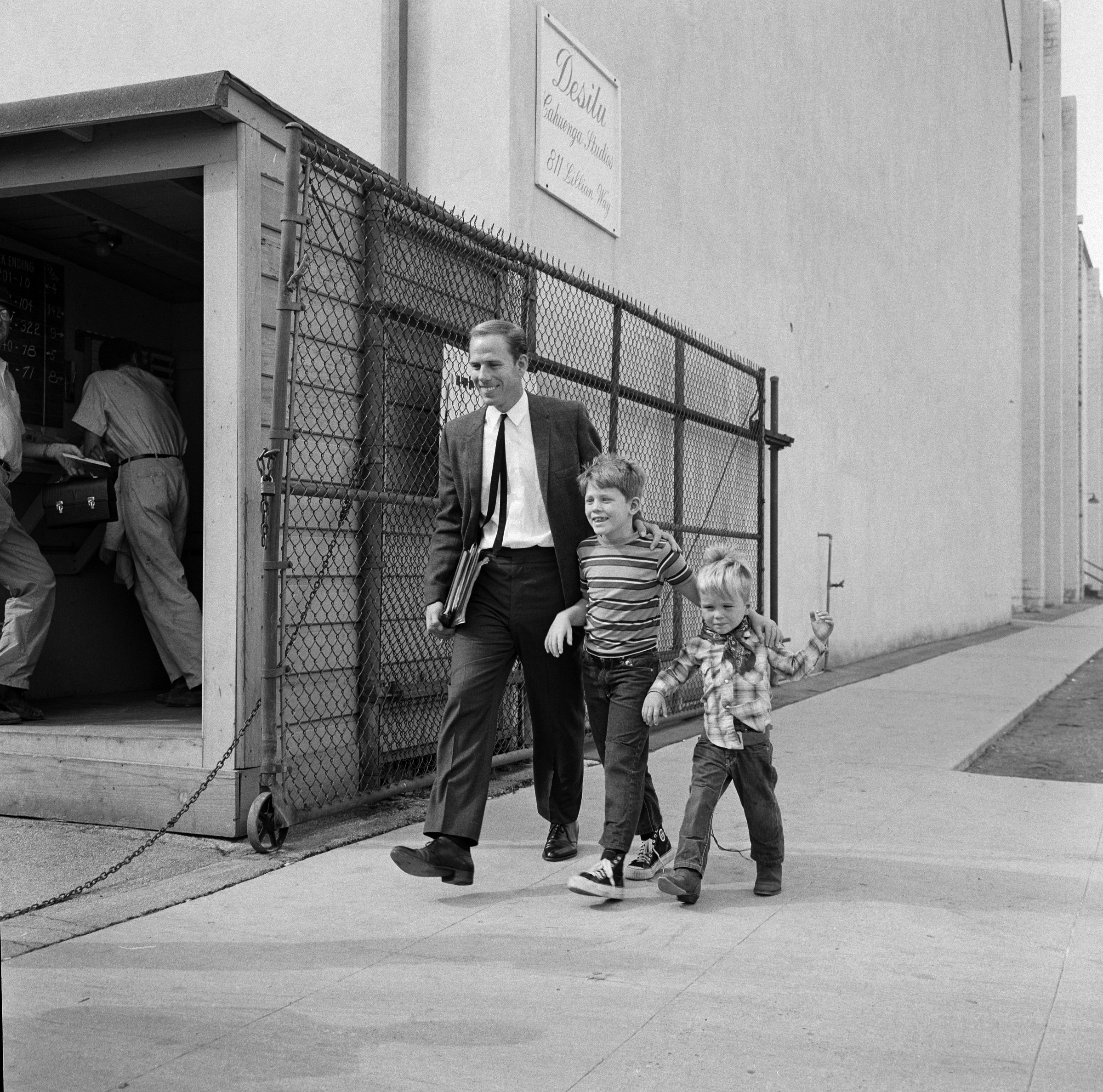Left to right: Rance Howard is in a dark suit and tie, walking with his young sons Ron Howard and Clint Howard on 'The Andy Griffith Show' set in 1963.