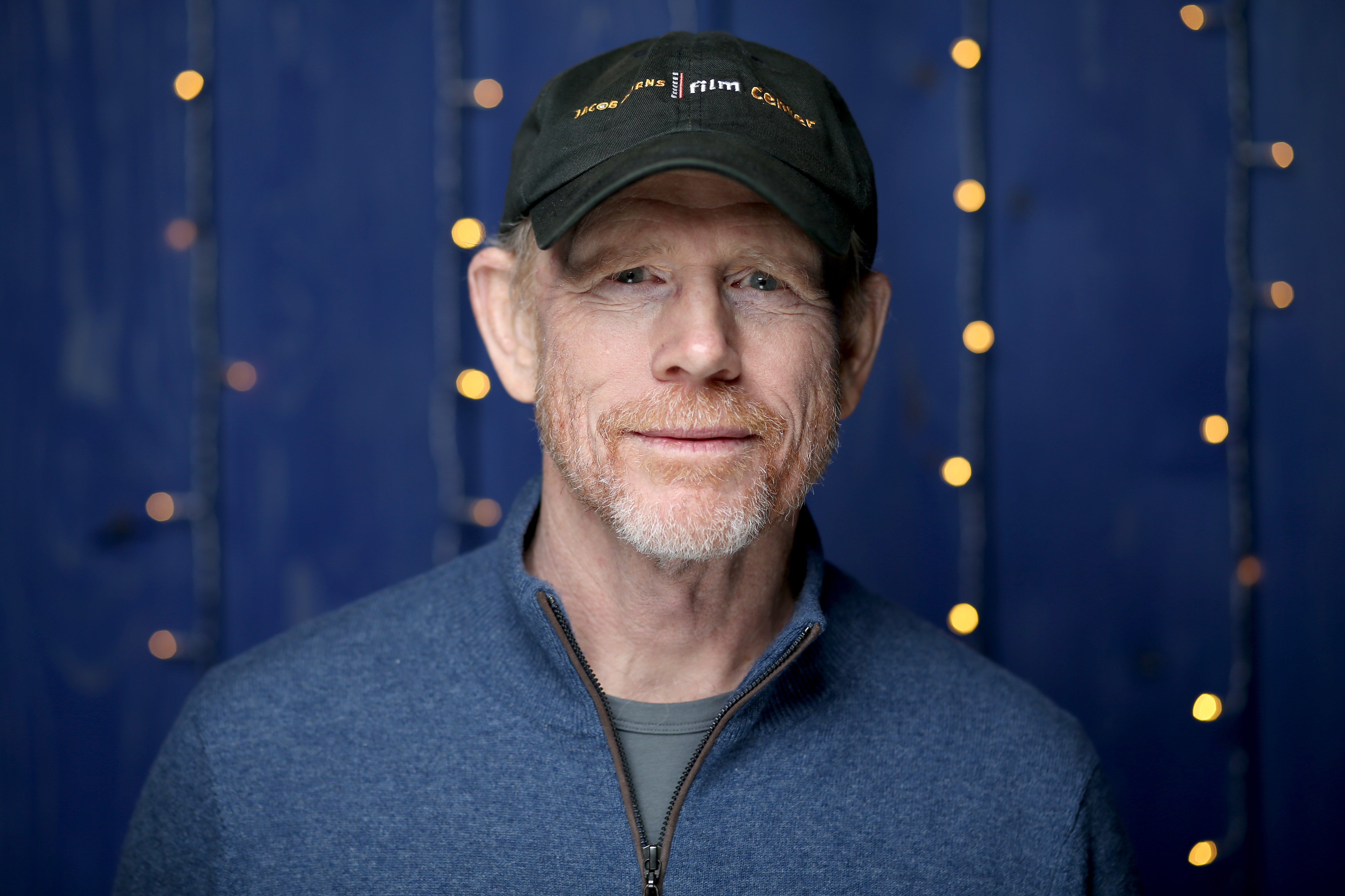 Filmmaker and actor Ron Howard poses for a photograph wearing a ballcap and blue zippered top.