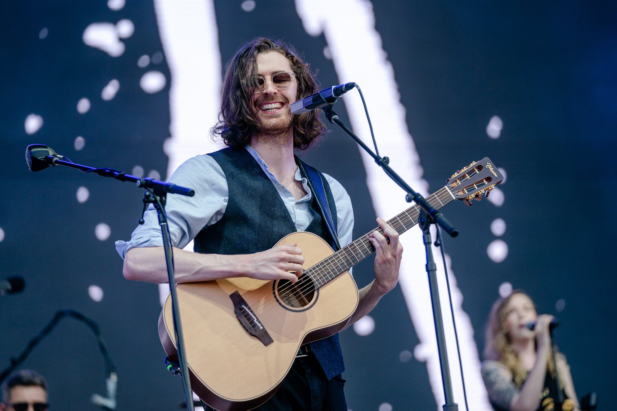 Hozier smiling, holding a guitar, on stage