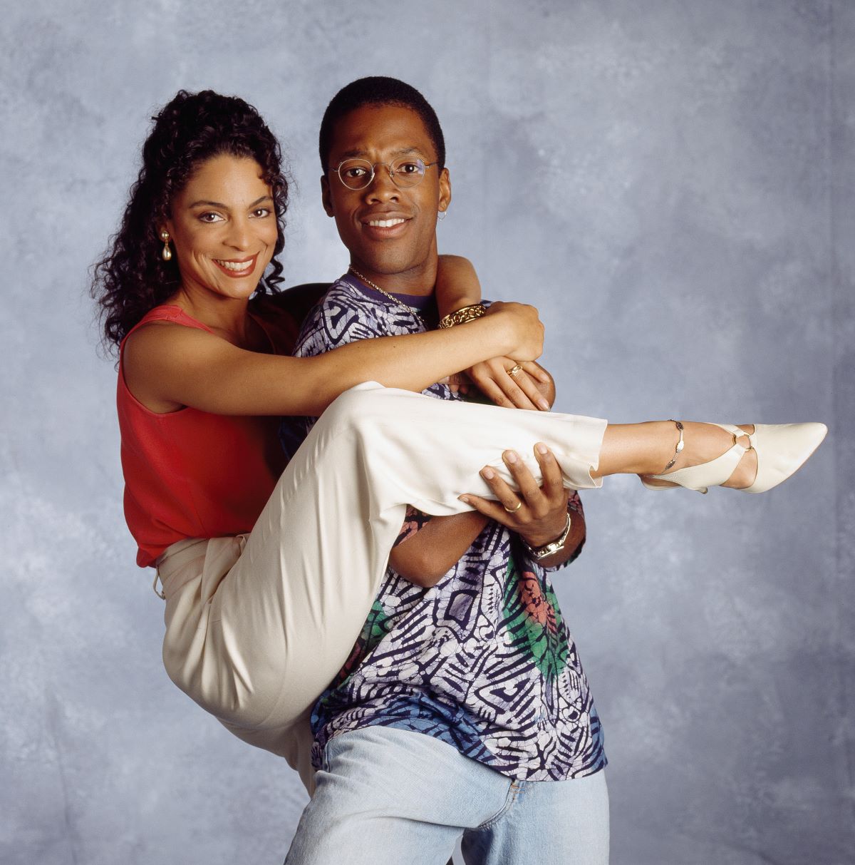 'A Different World' stars Jasmine Guy in a red tank top and khaki pants as Whitley Marion Gilbert Wayne and Kadeem Hardison holding Jasmine