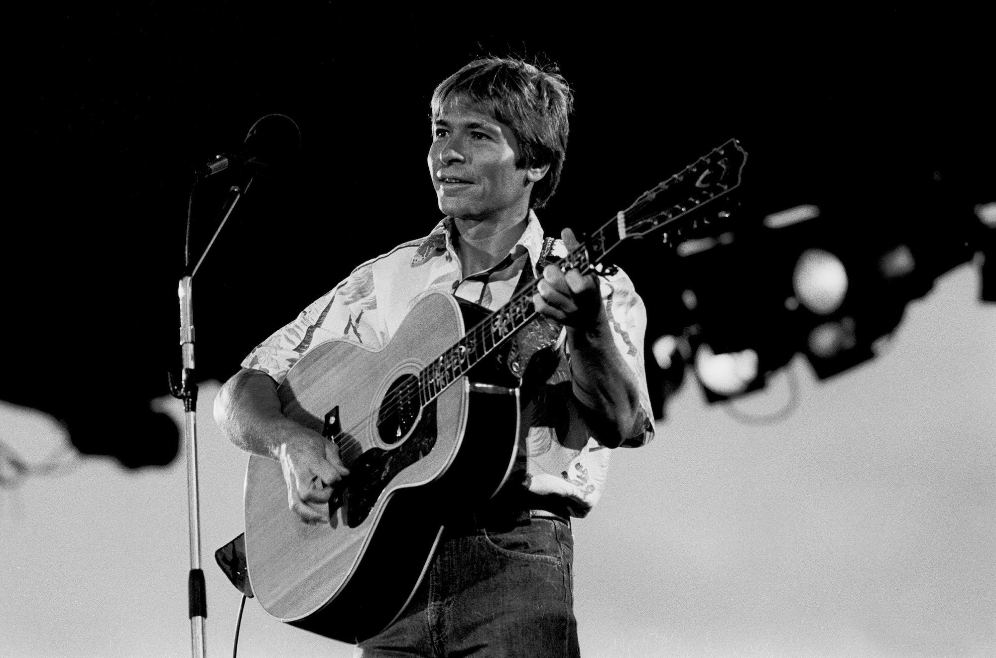 John Denver smiling, performing on stage, in black and white