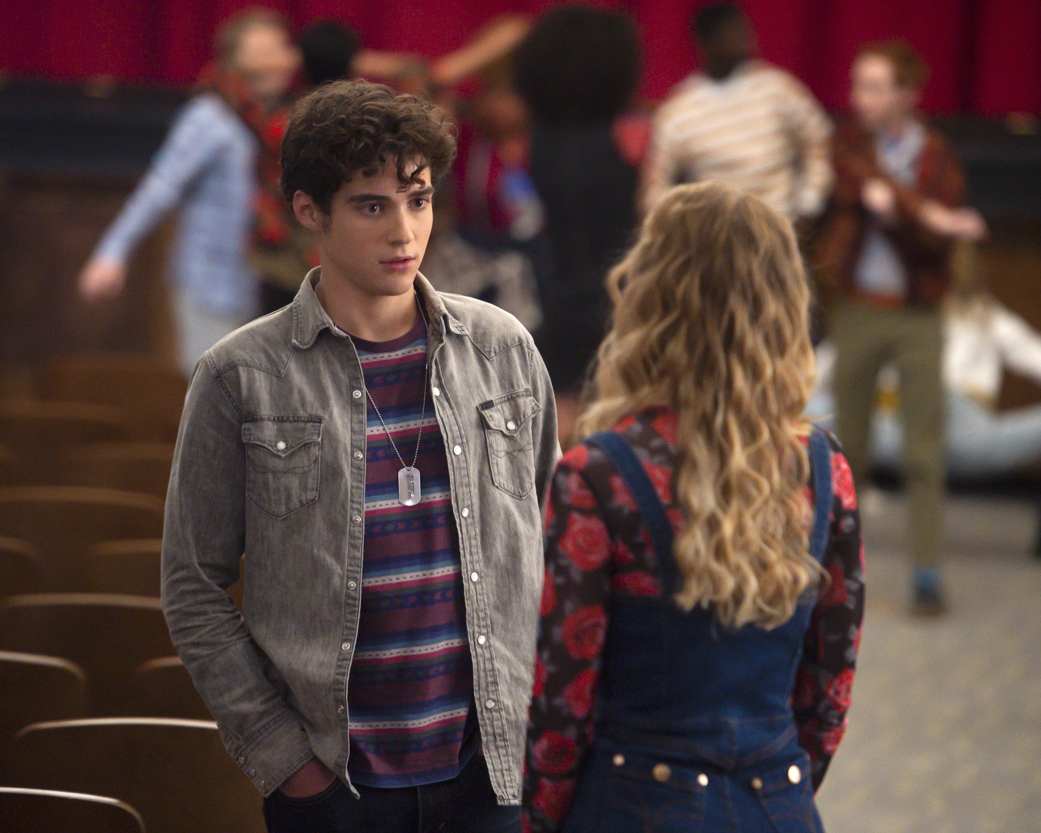 Joshua Bassett in the Disney+ original series 'High School Musical: The Musical: The Series' as Ricky Bowen, dressed in a gray jacket talking to another character