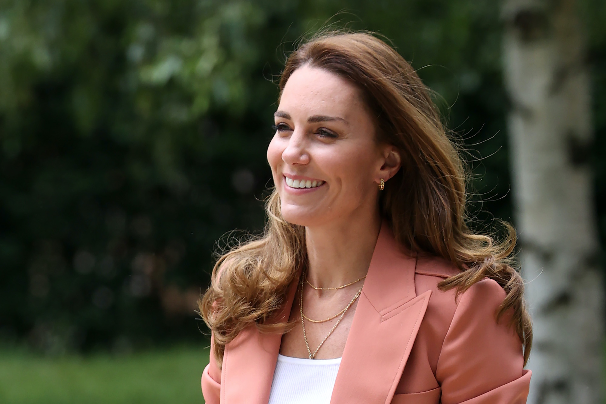 Duchess of Cambridge Kate Middleton smiling, looking off camera in a salmon-colored blazer