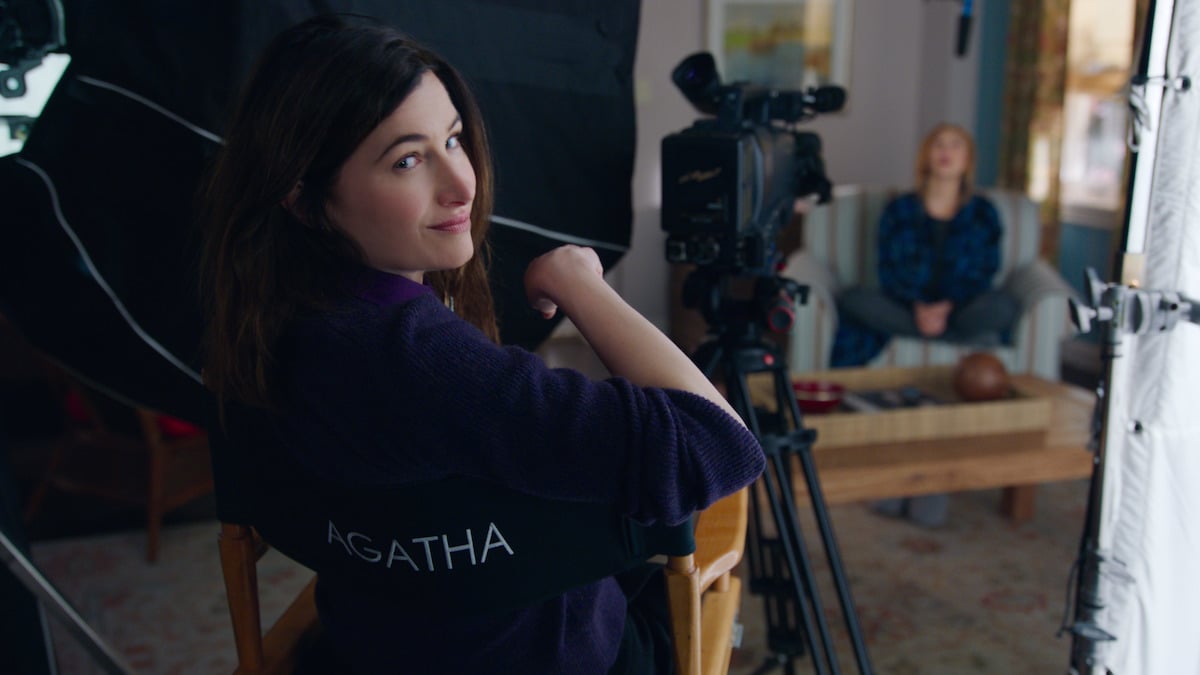 Agatha Harkness (Kathryn Hahn) sits in a director's chair and turns to camera smiling in 'WandaVision'