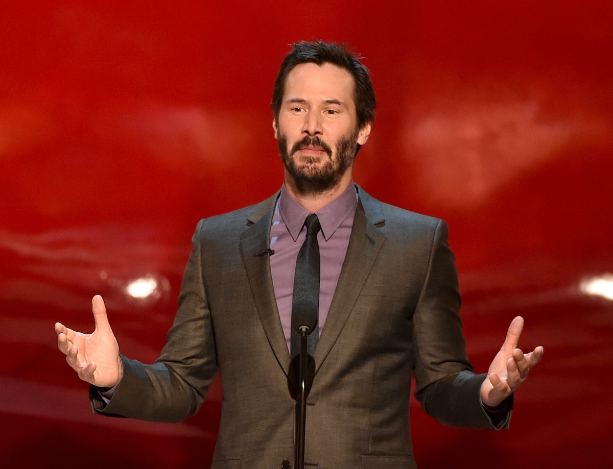 Keanu Reeves stands onstage in a suit