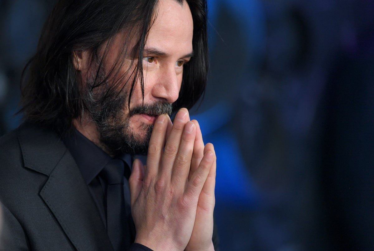 Keanu Reeves wears black and holds his hands to his lips