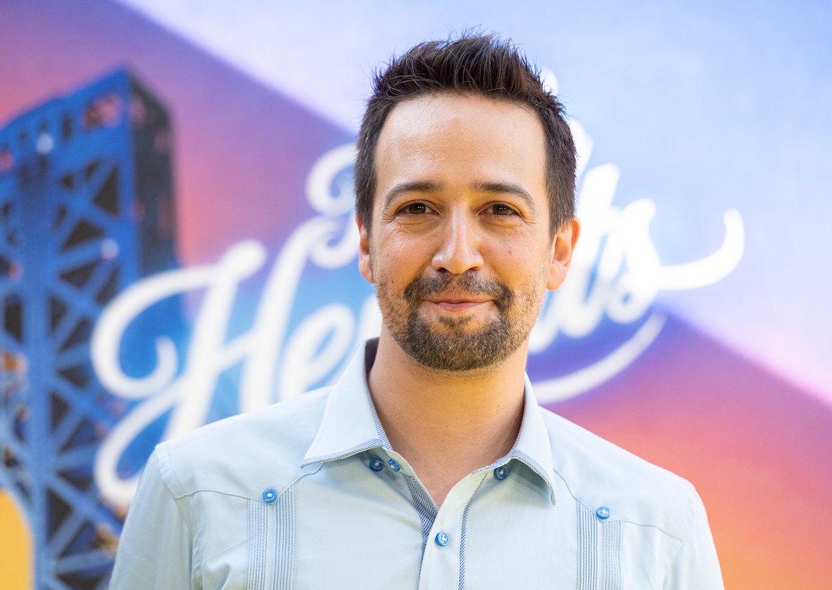 Lin-Manuel Miranda smiles and poses in front of a display of 'In The Heights'