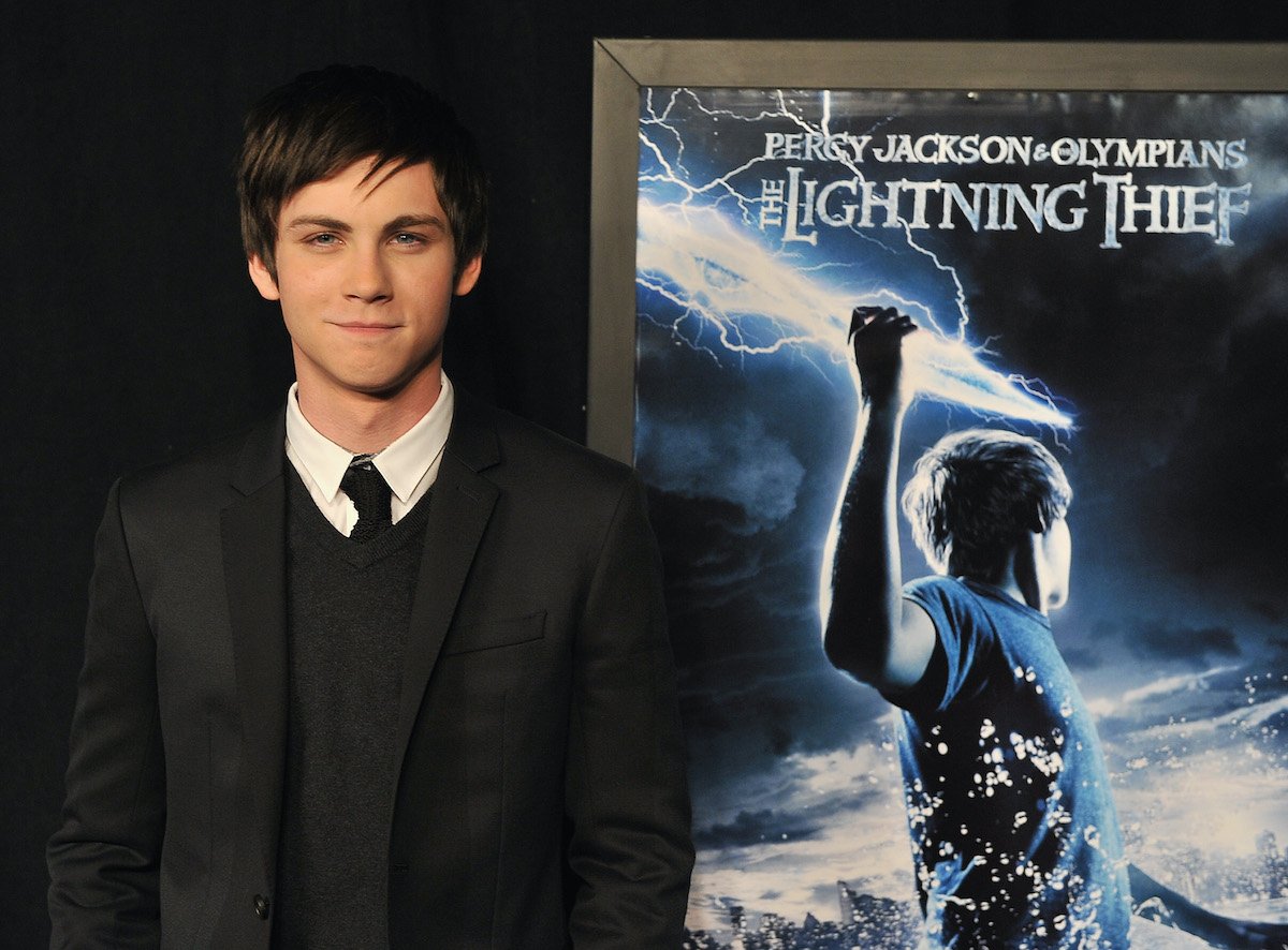 Logan Lerman wears a black suit and tie at the premiere of 'Percy Jackson and The Olympians: The Lightning Thief' in 2010. He stands in front of a blue and white poster for the film, which shows him holding a lightning bolt.